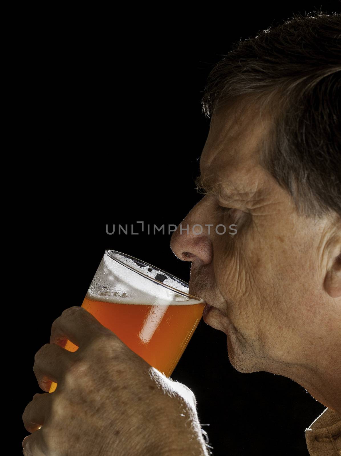 Senior caucasian man in profile drinking from a pint glass of beer or lager