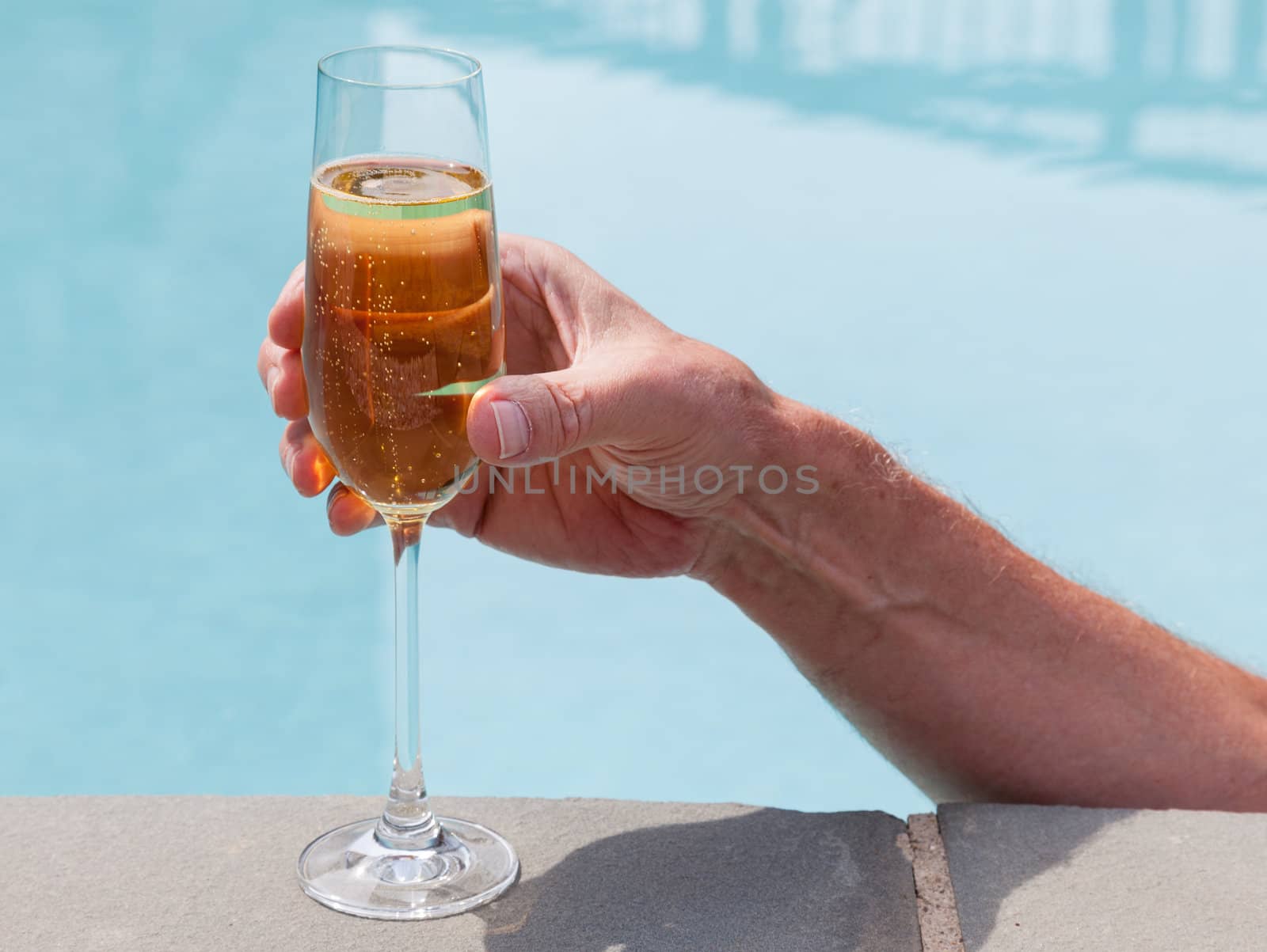 Elegant flute glass of sparkling white wine or champagne being held from in pool