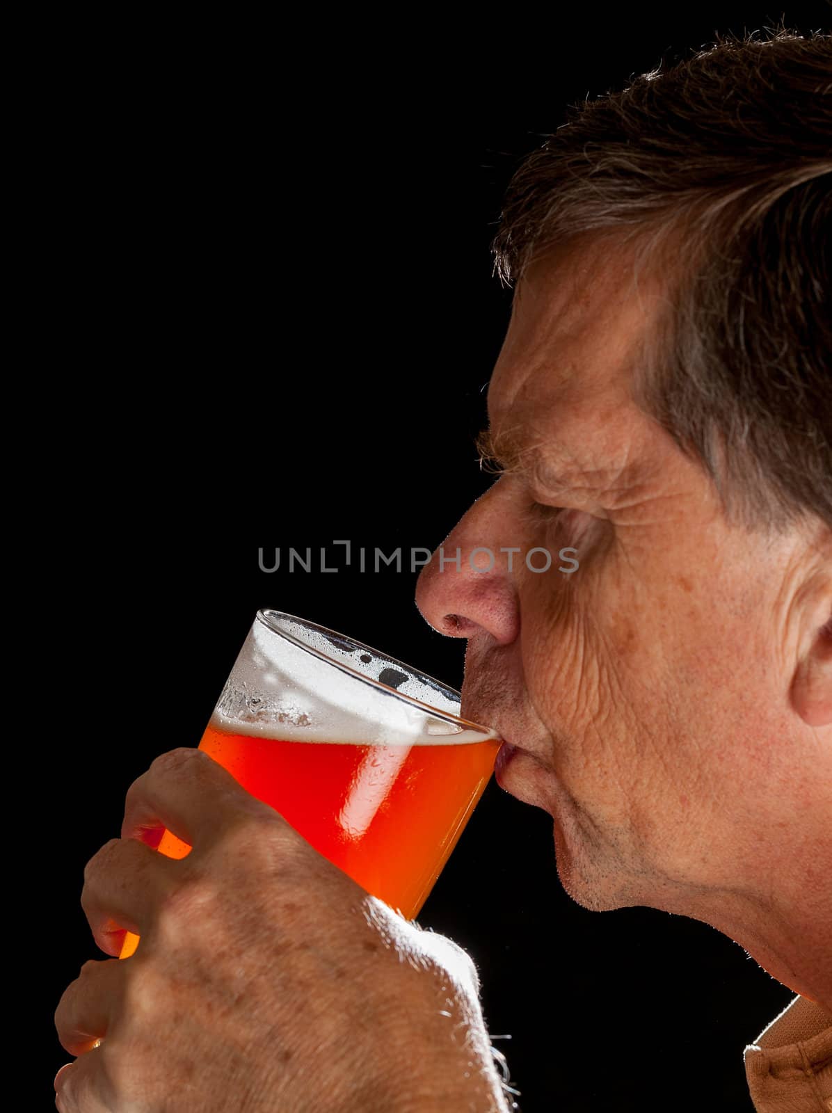 Senior caucasian man in profile drinking from a pint glass of beer or lager