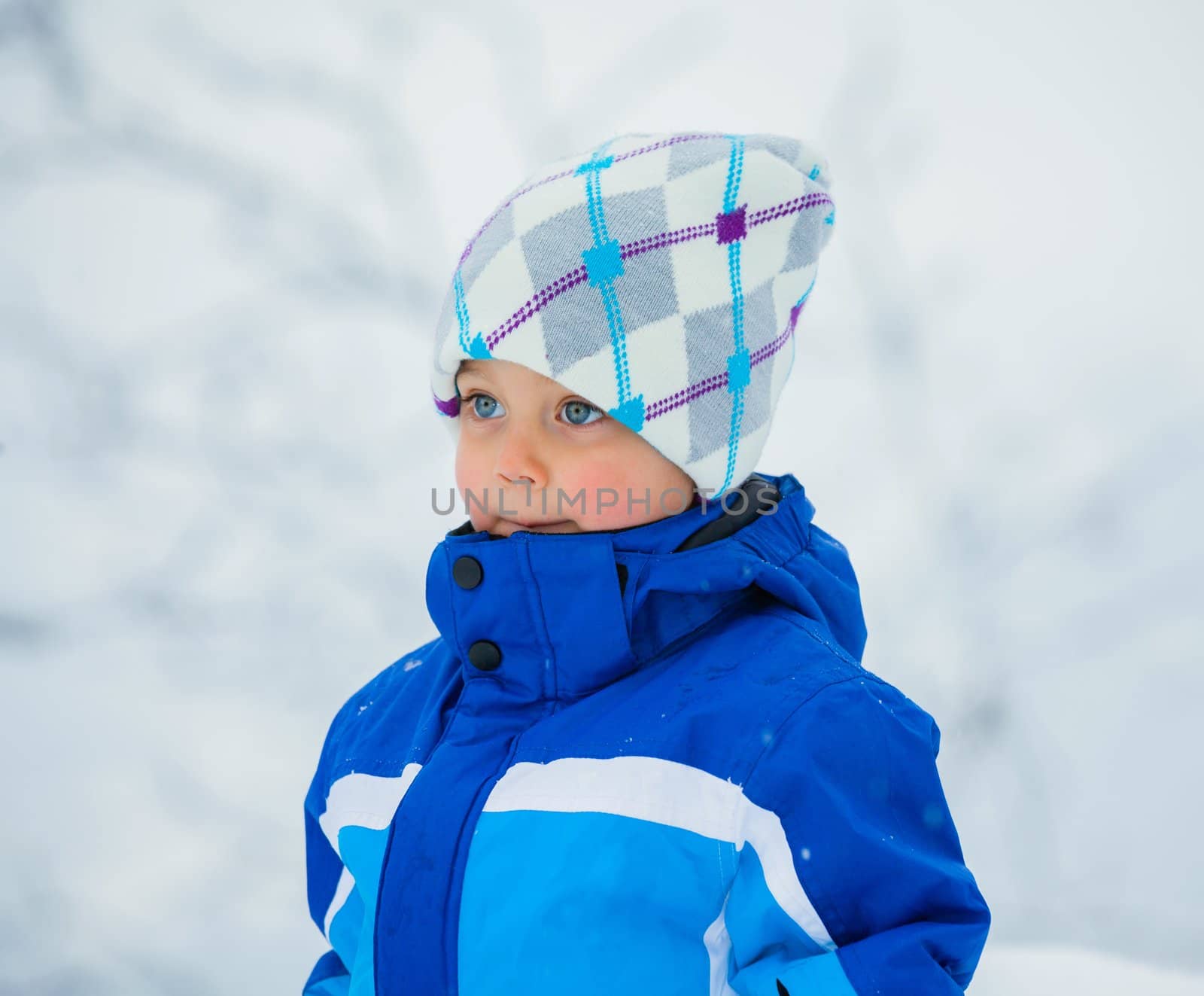 Smiling happy boy having fun outdoors on snowing winter day in Alps playing in snow.