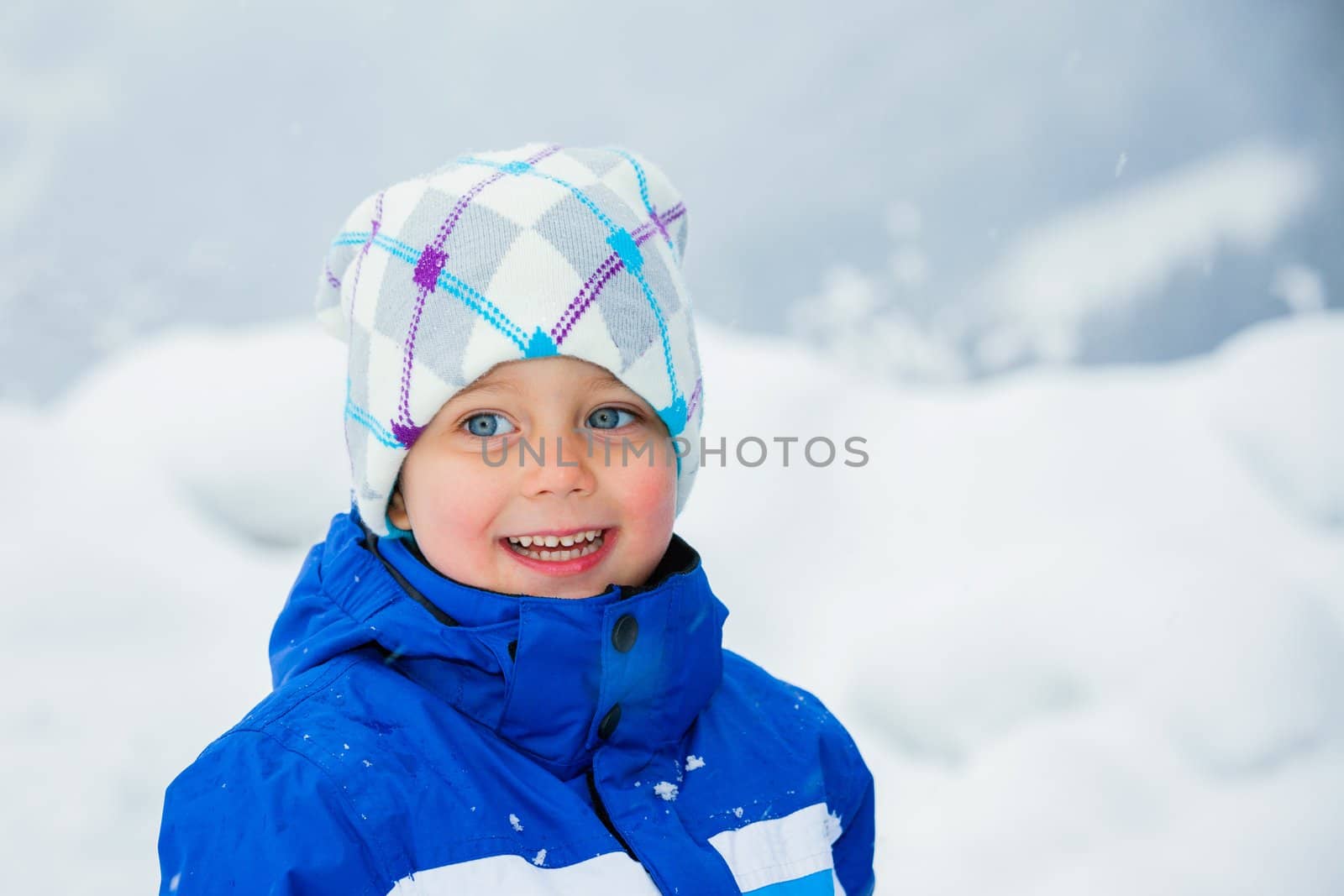 Smiling happy boy having fun outdoors on snowing winter day in Alps playing in snow.