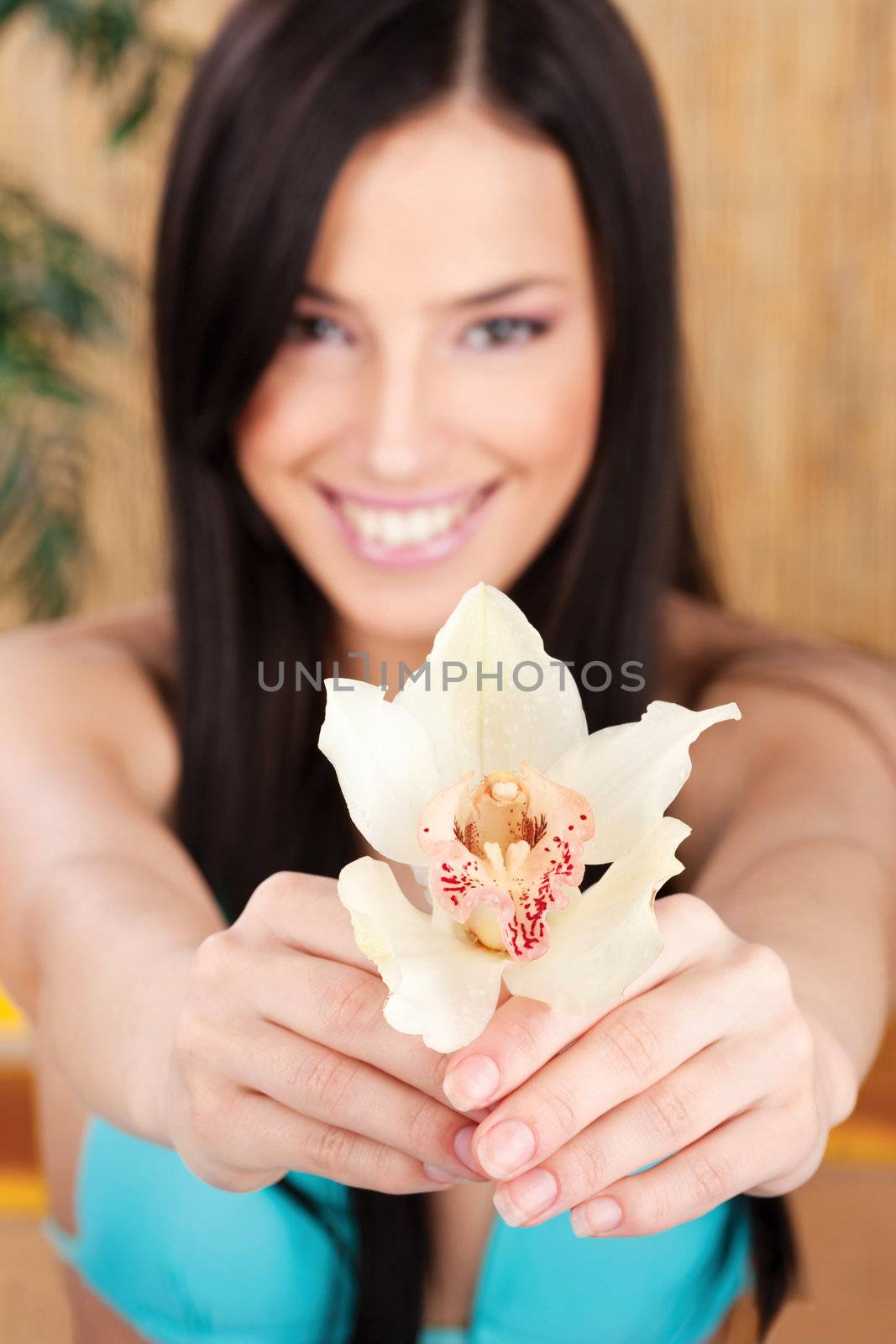 Pretty smiled woman holding white orchid in bikini, focus on flower
