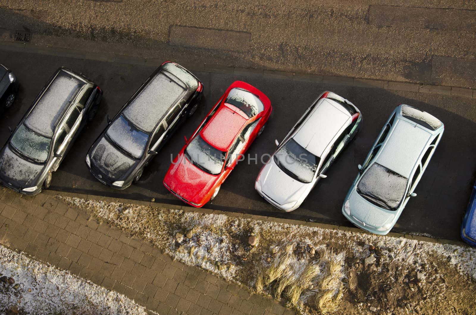 Cars covered with snow stand in parking shot from roof in winter.