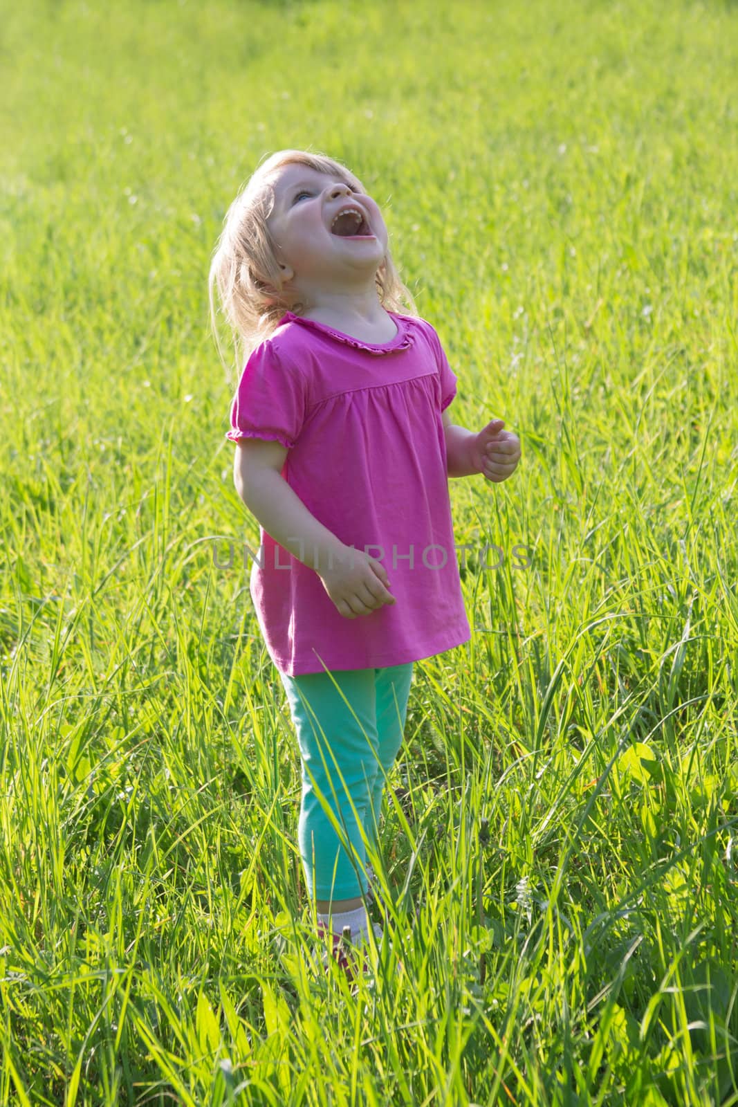 Joyful baby girl looking up among grass