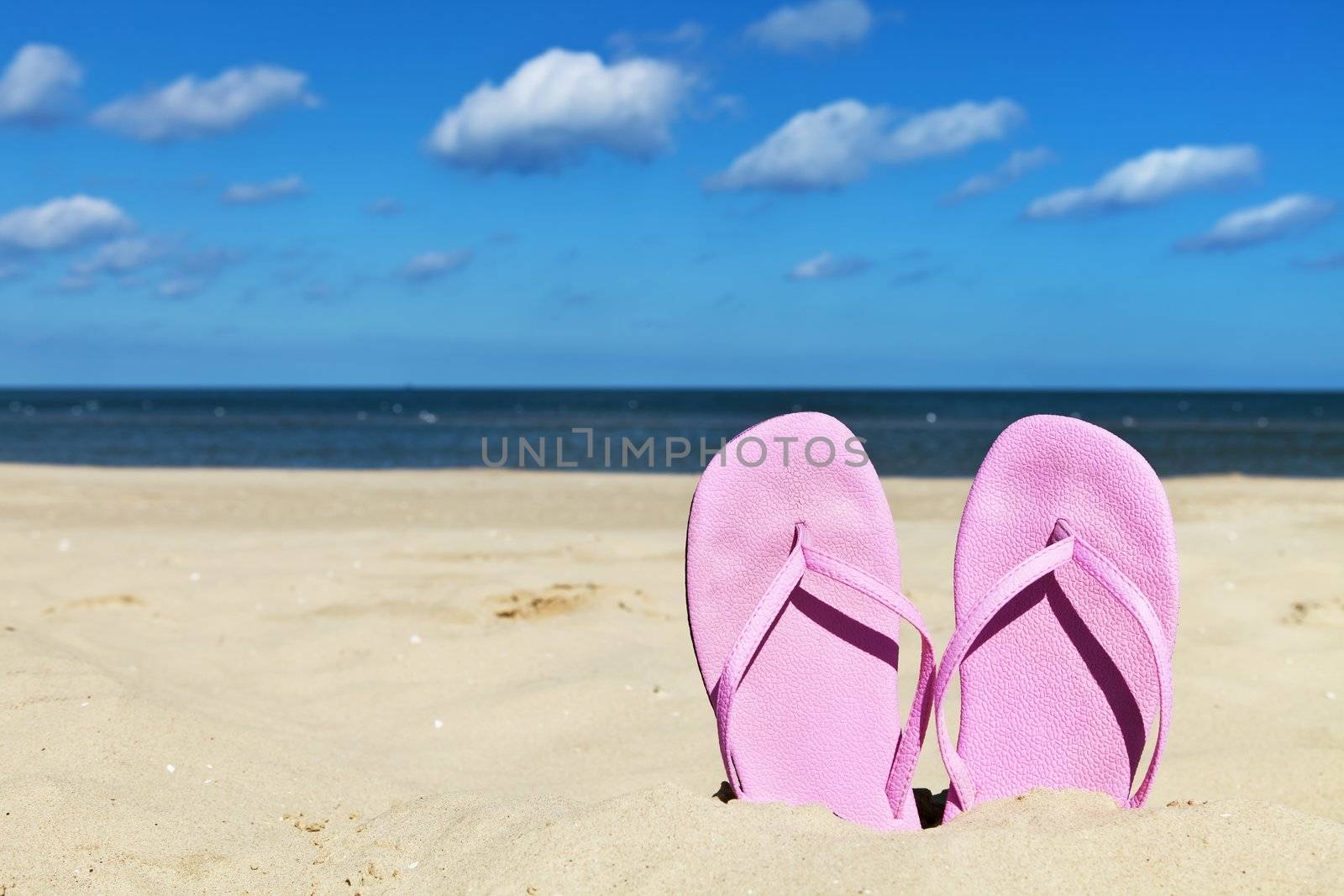 Women's pink flip flops alone on sandy beach