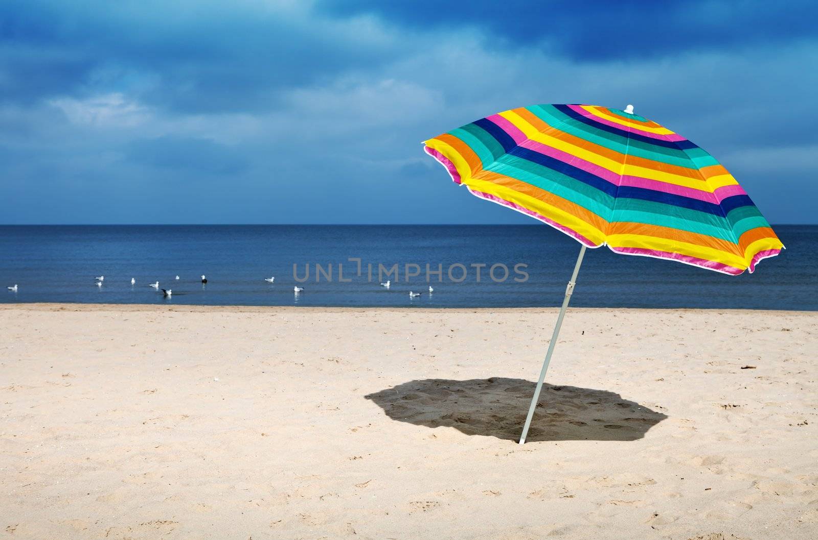 Colorful umbrella on a sandy beach, peaceful sea in a background