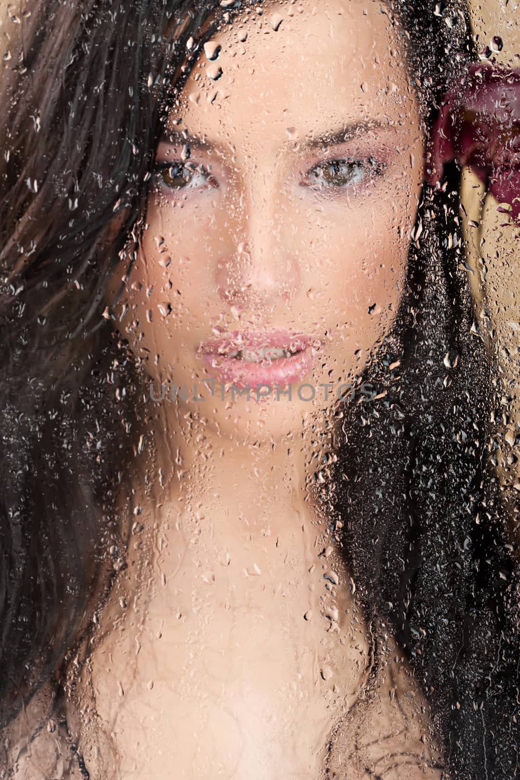 Close up of a pretty woman's face behind glass full of water drops