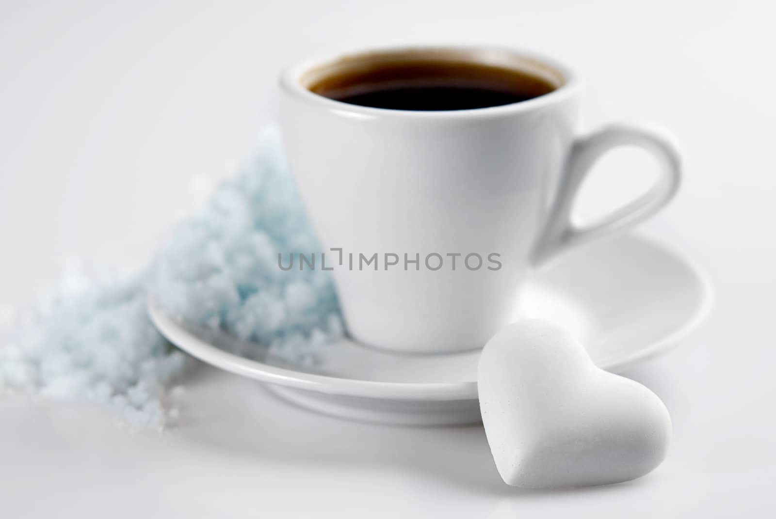 Cup of coffee with heart shaped blank candy and snow hill on saucer. Isolated on white. Small Depth of Field