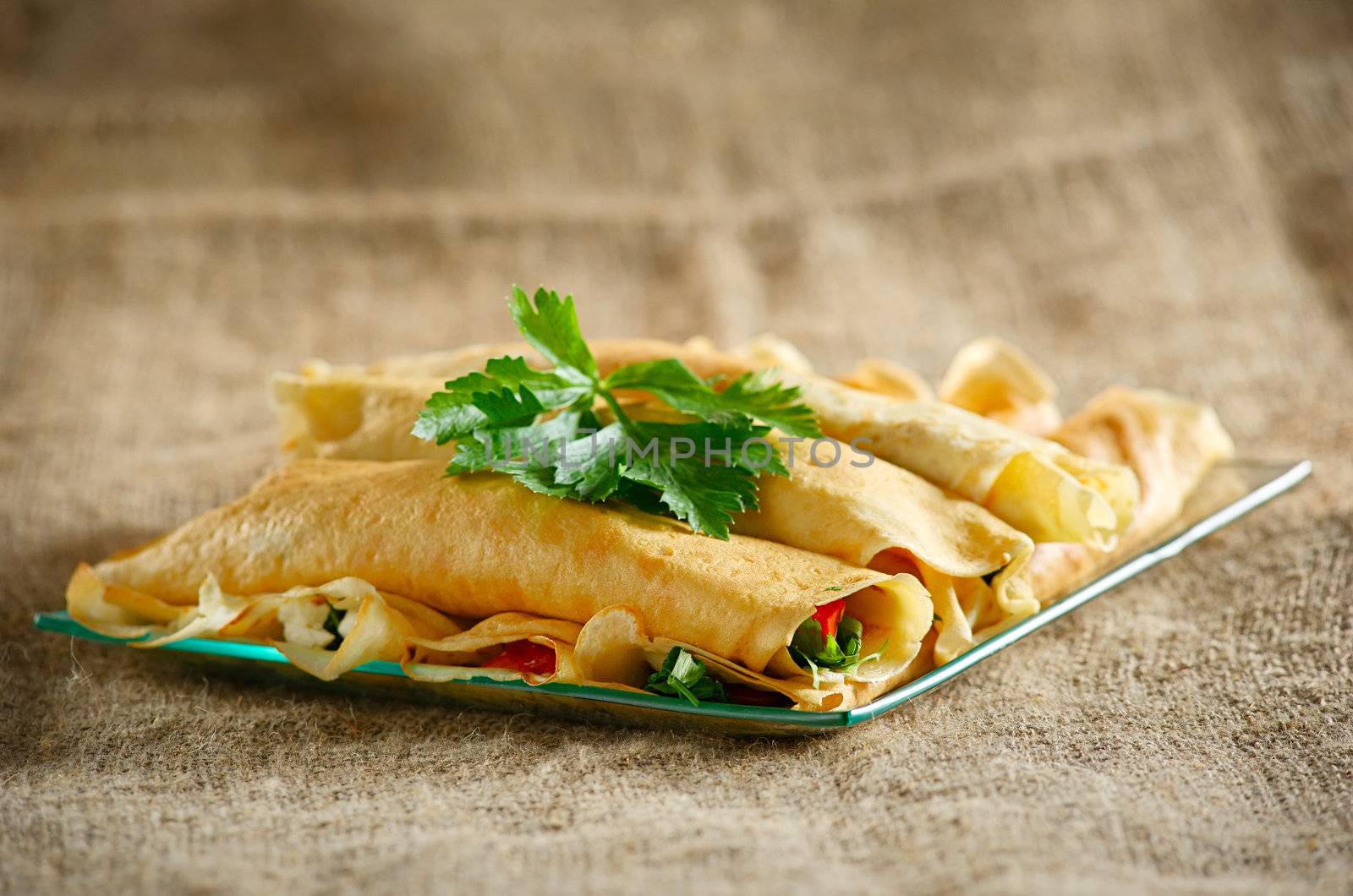 Dessert with the rolled pancakes in a glass plate on the background of canvas cloth