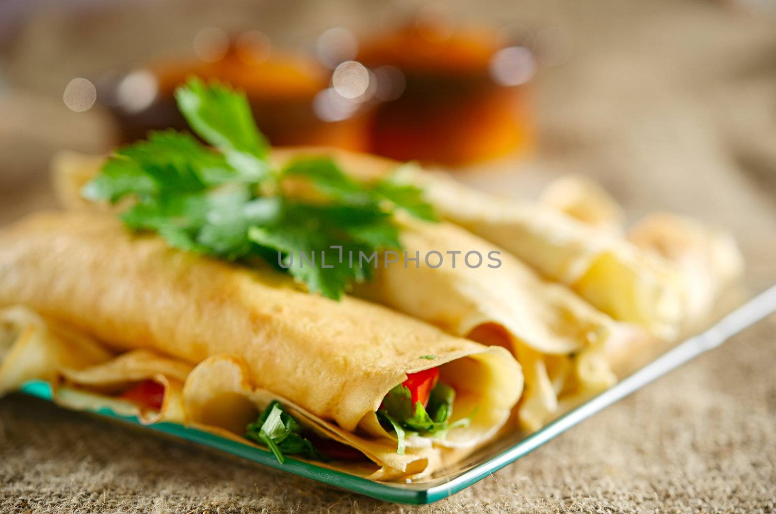 Dessert with the rolled pancakes in a glass plate on the background of canvas cloth