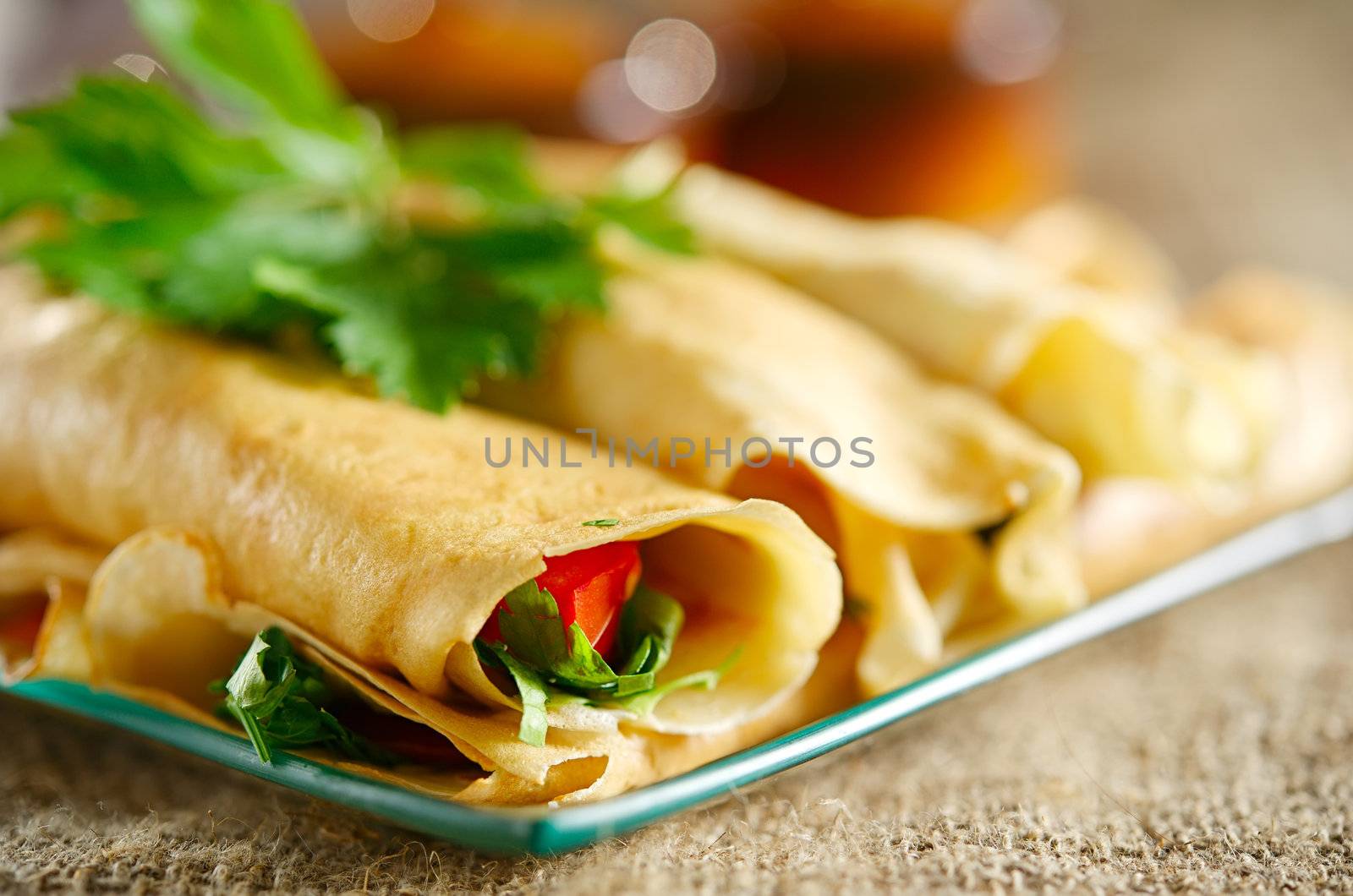 Dessert with the rolled pancakes in a glass plate on the background of canvas cloth