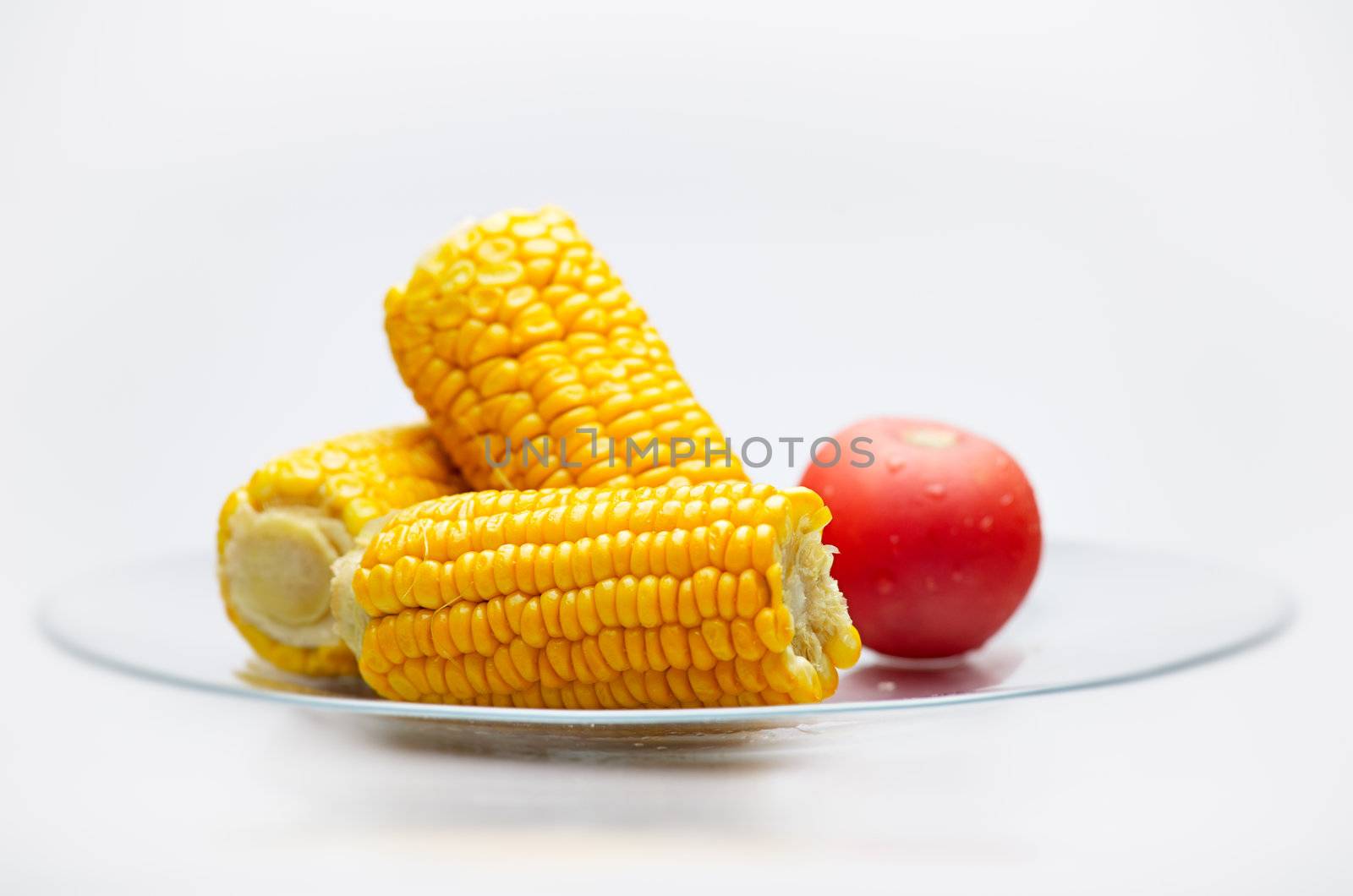 Still life of Corn Cobs and tomato on a glass plate. Isolated on White background. Small Depth of  Field.