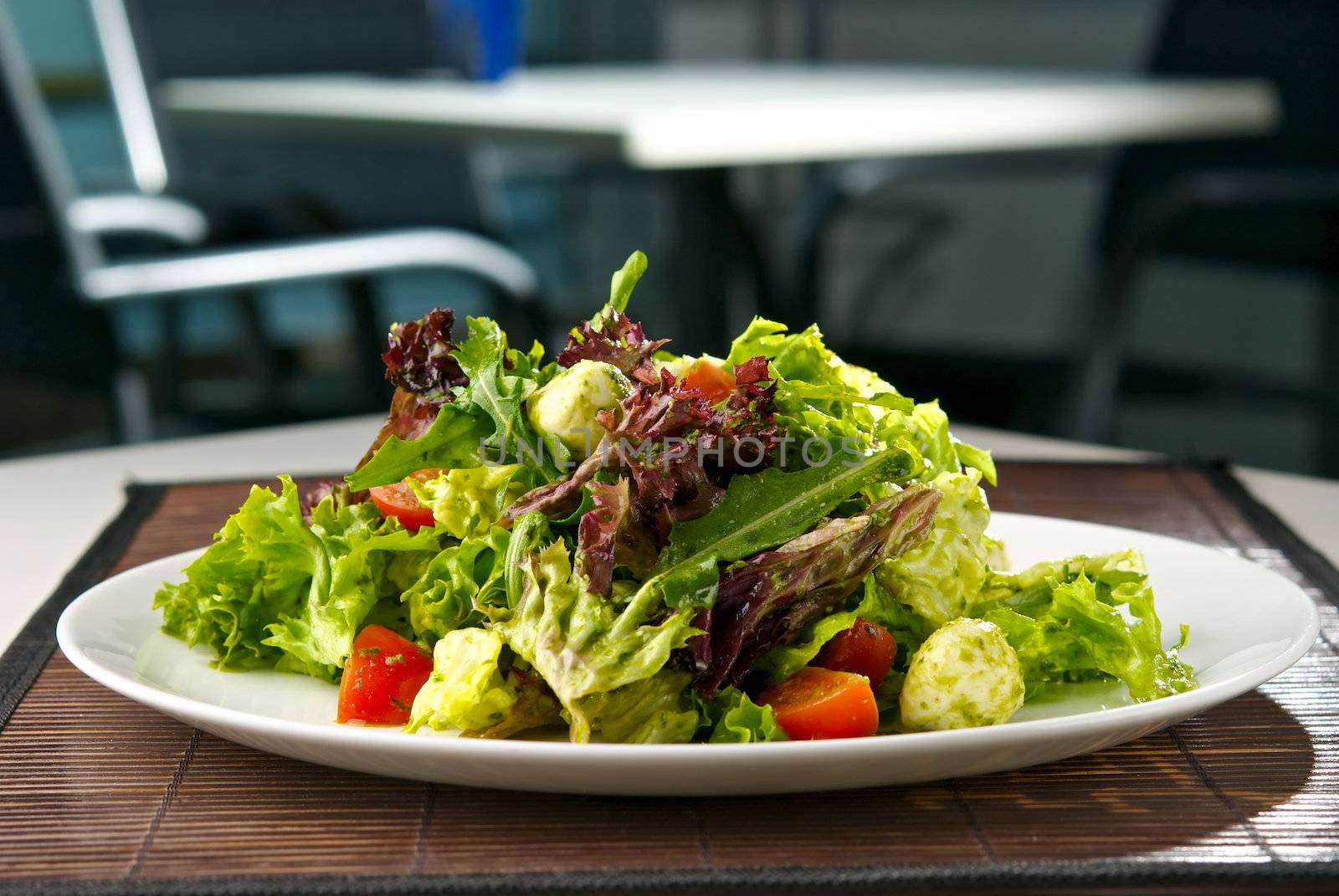 Fresh salad with mozzarella cheese and cherry tomatoes. Indoor. Blurry background of restaurant interior