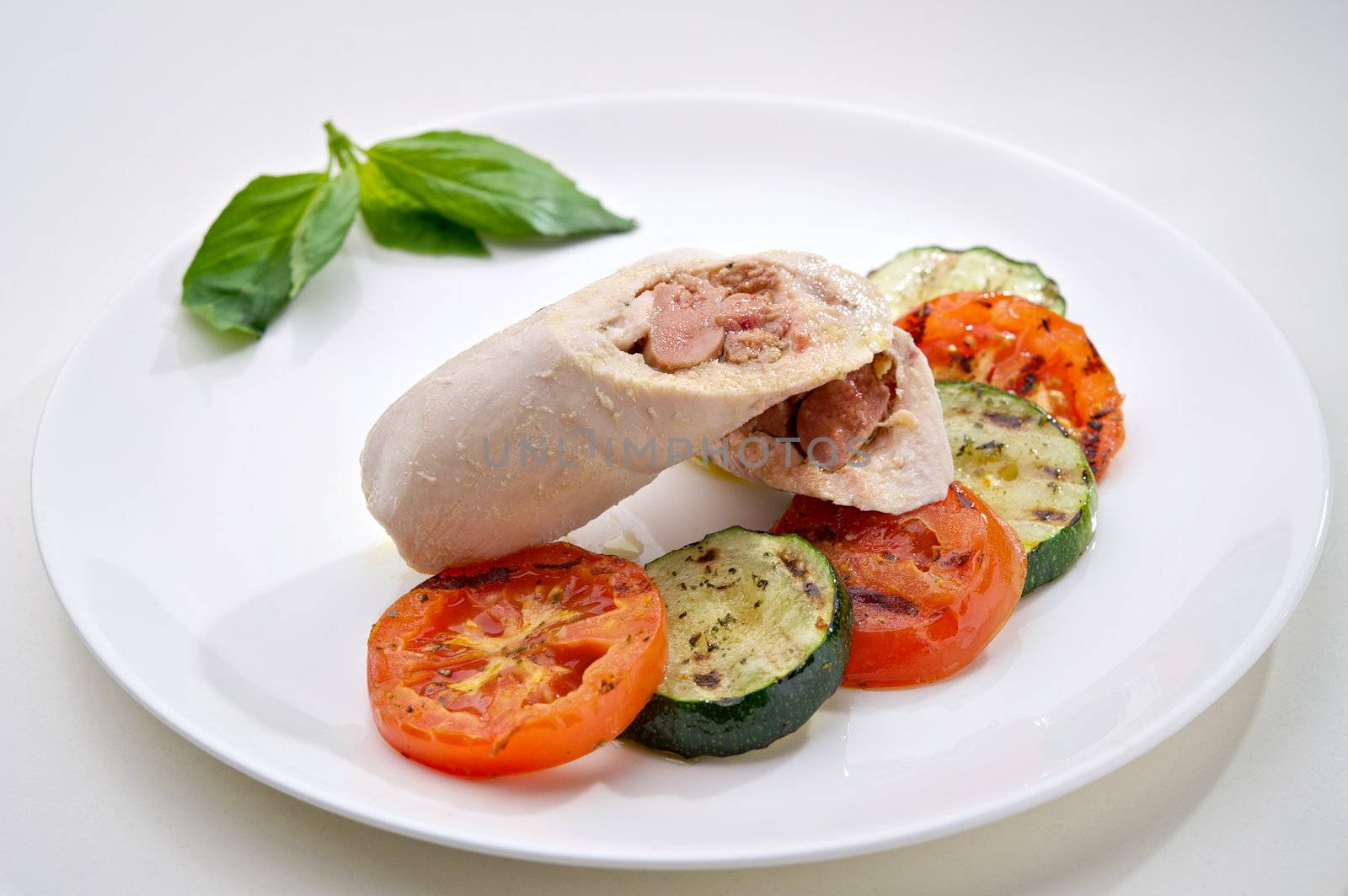 Steamed chicken cutlets served with baked vegetables on round white plate