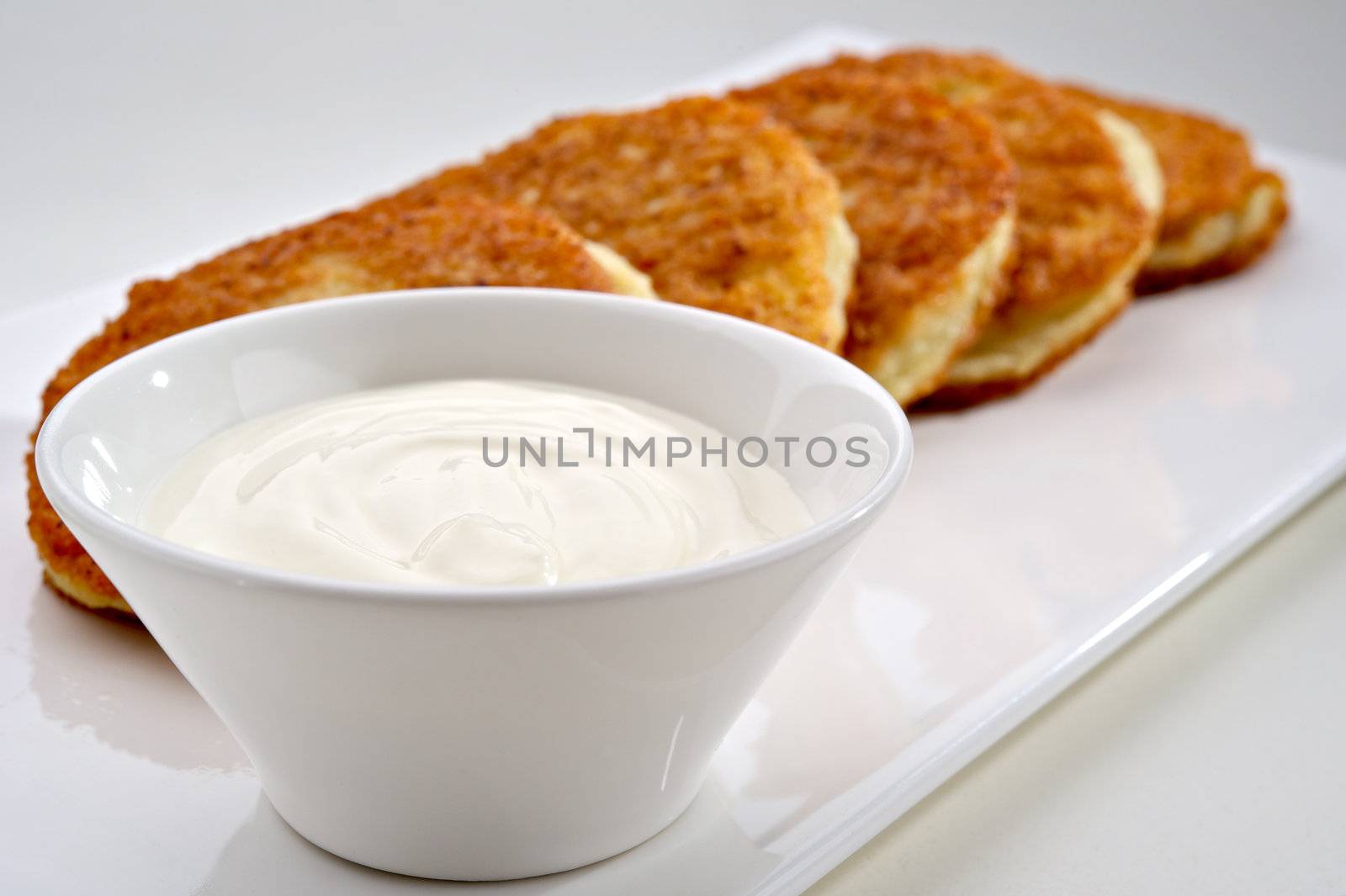 Potato pancakes served on white plate with sour cream