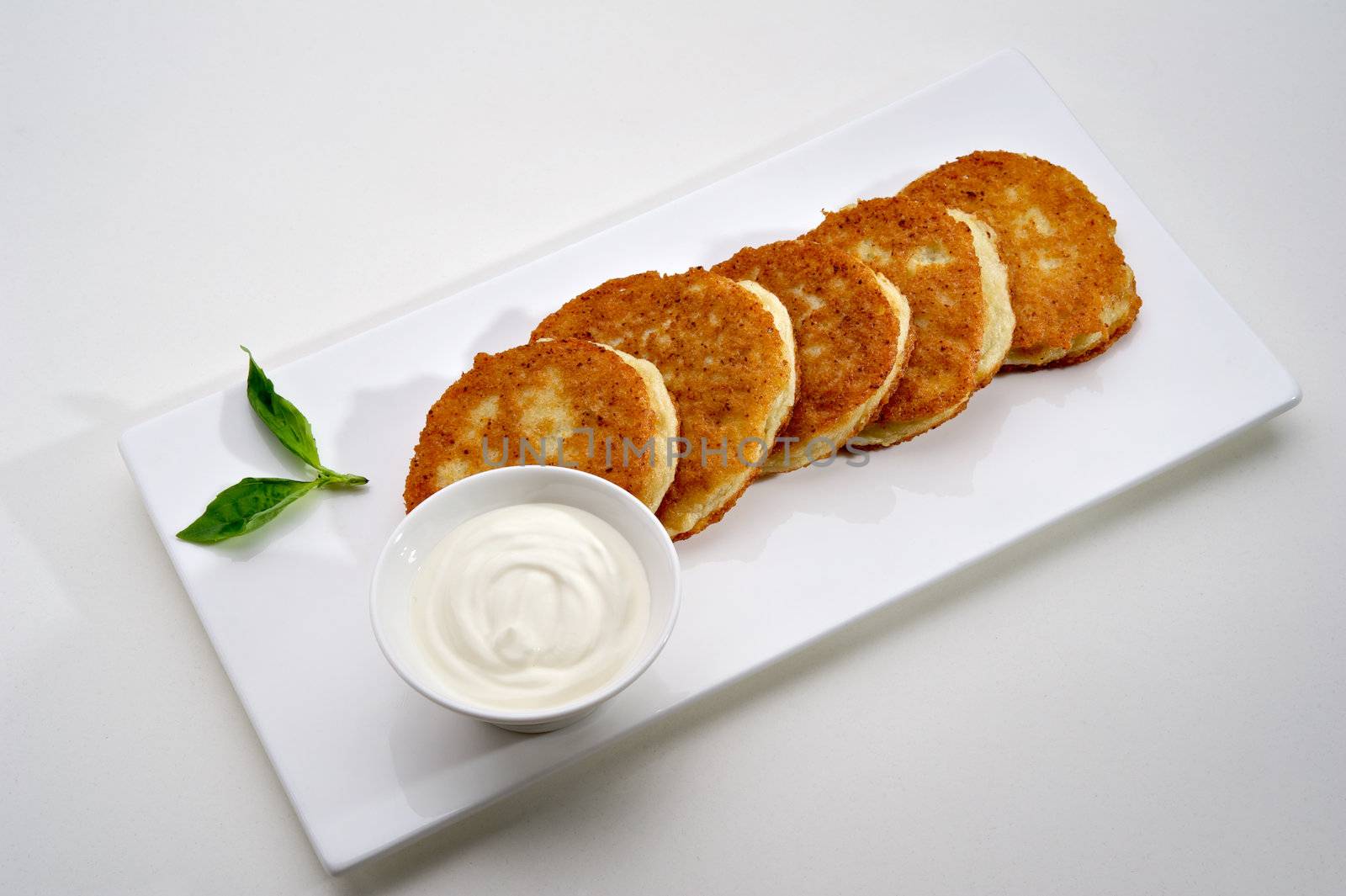 Potato pancakes served on white plate with sour cream