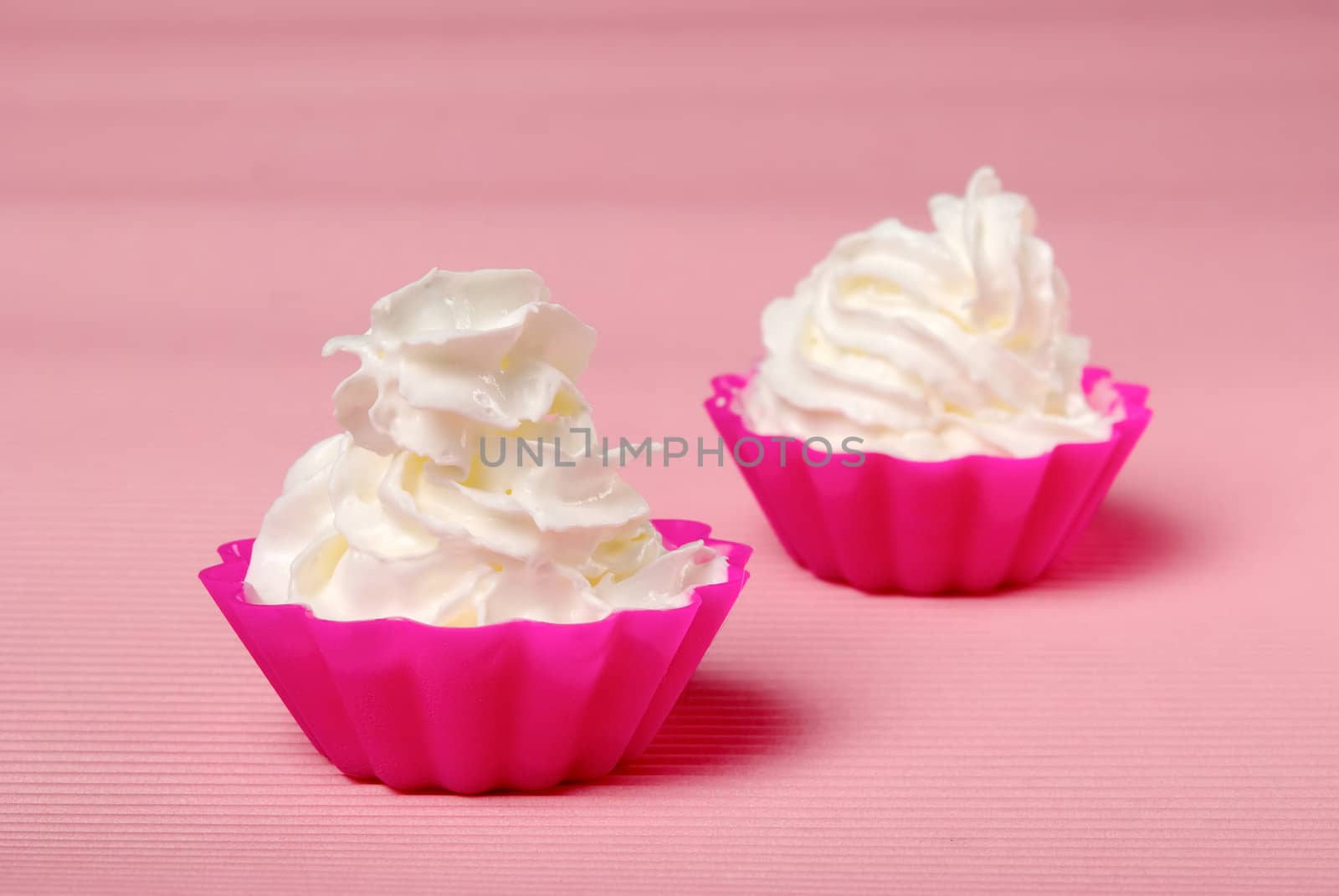 Two portions of whipped cream over pink background. Shallow DOF