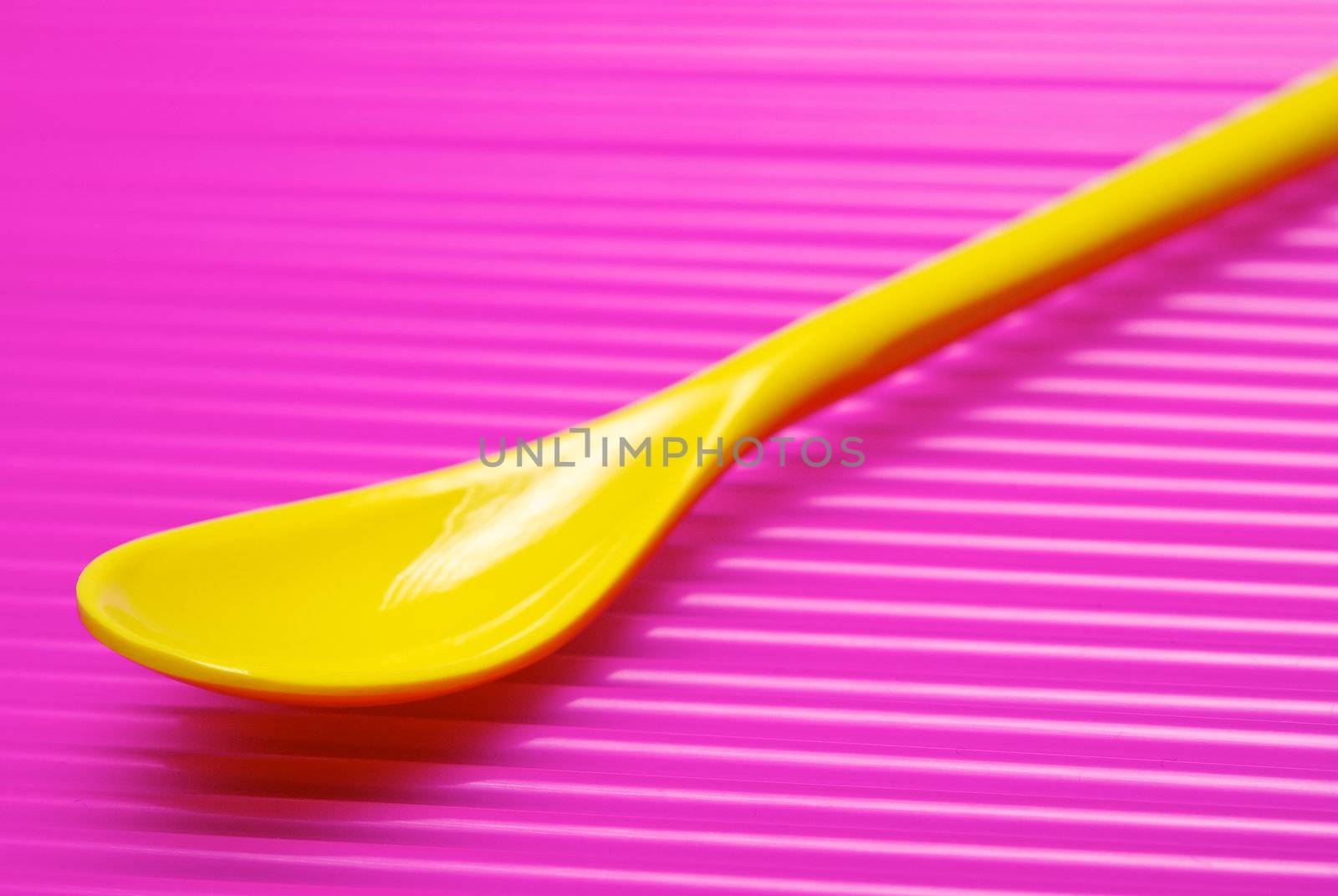 Single empty yellow desert spoon on abstract pink background.