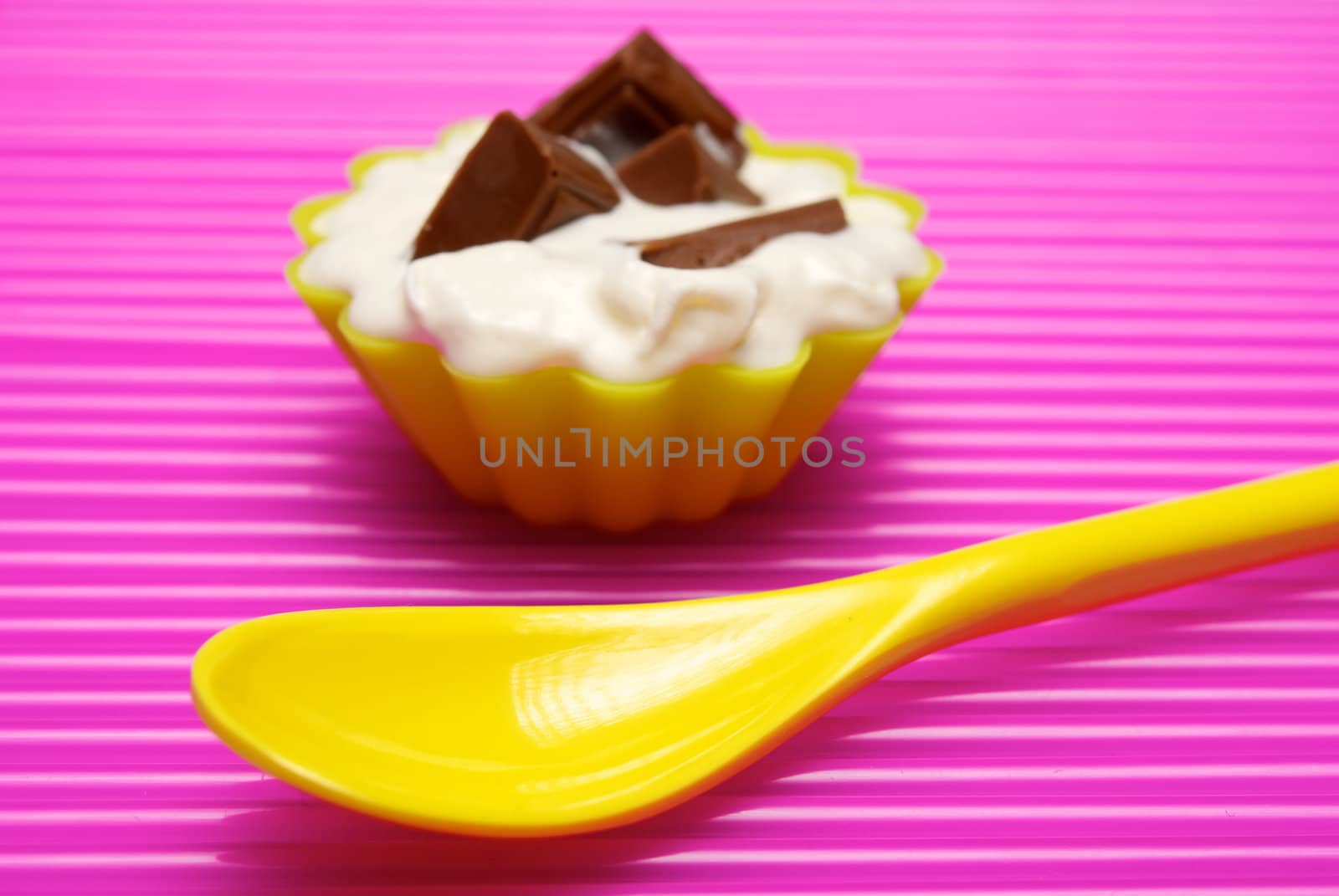 Empty yellow spoon with portion of whipped cream and chocolate over pink background. Shallow DOF