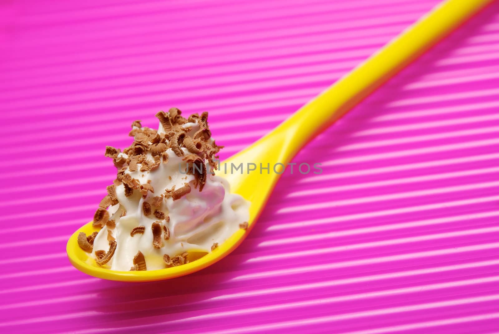 Yellow spoon full of whipped cream with chocolate shavings over pink background. Shallow DOF