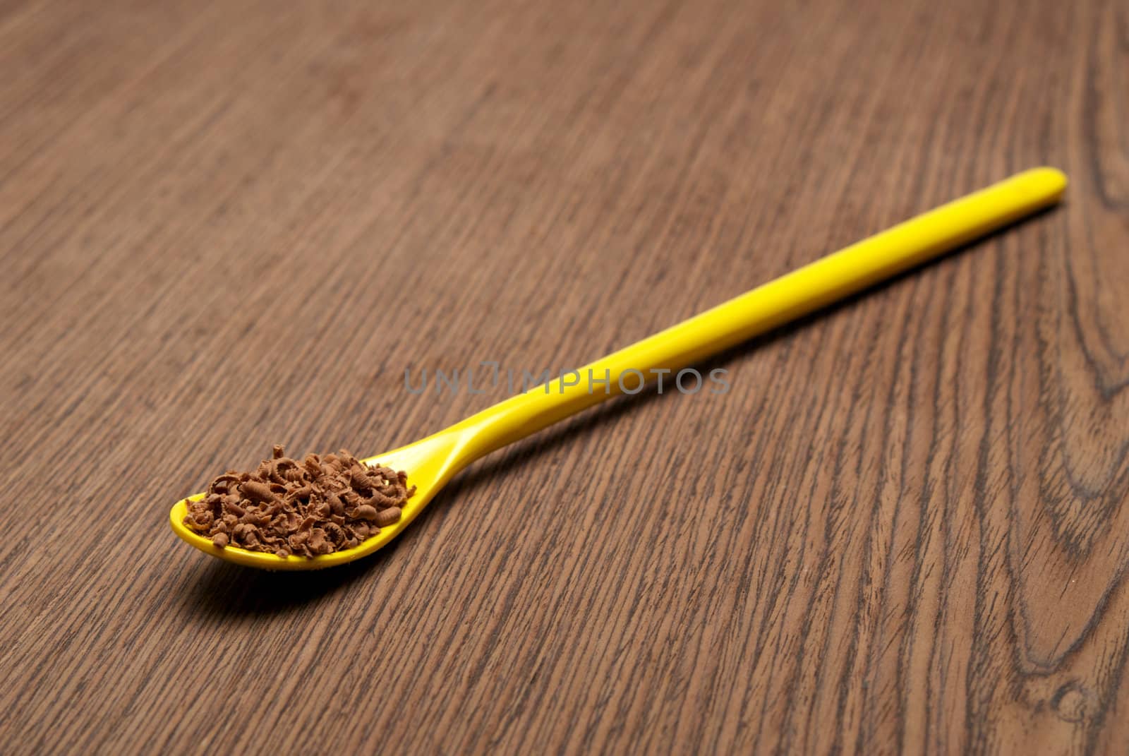 Teaspoon full of chocolate shavings, on a wooden background closeup