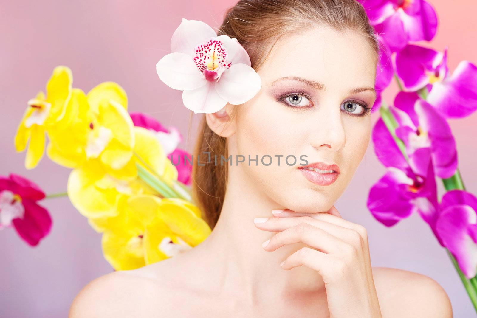 Pretty woman with orchid in her hair in front of flowers