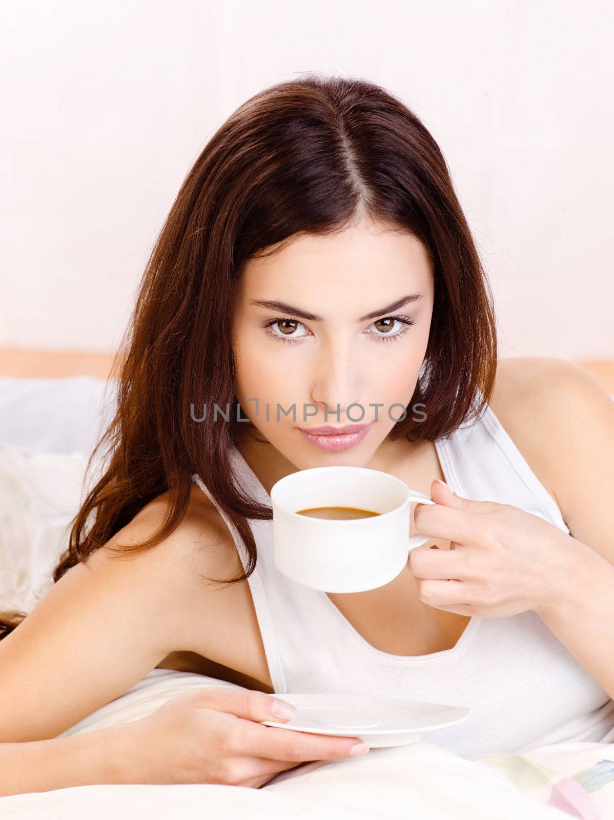 woman holding cup of coffee in bed by imarin