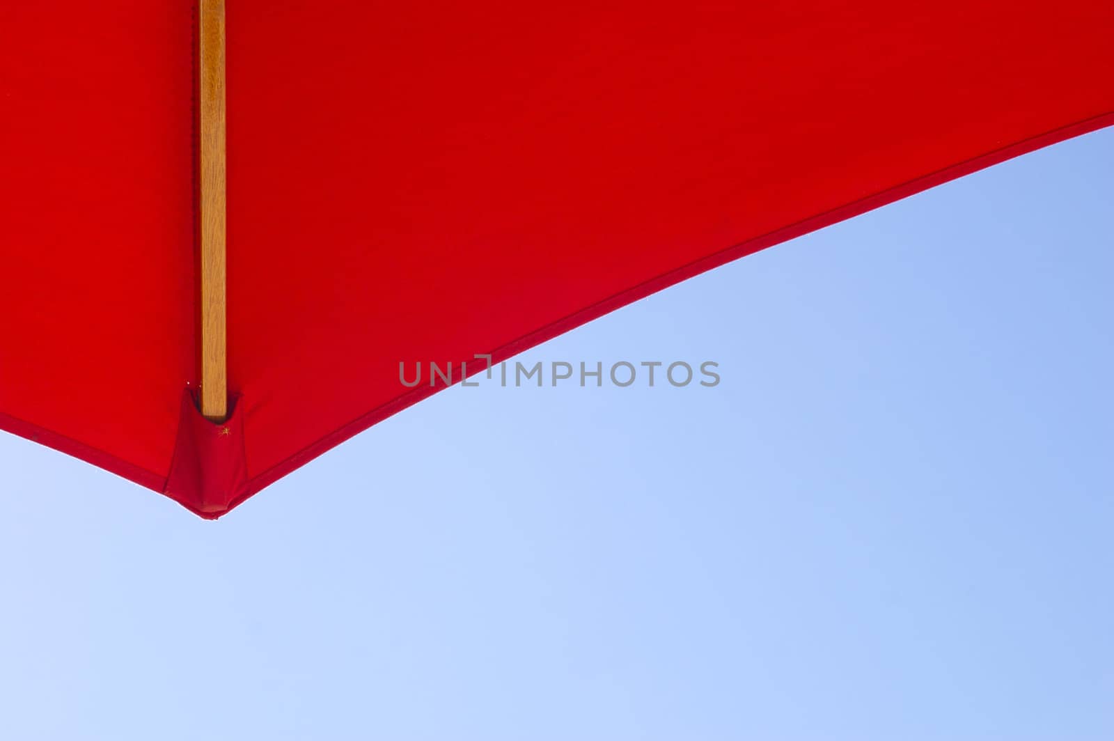 Point of a bright red sun umbrella/ sun-shade/ parasol against a bright blue sky, taken from beneath, as if looking up, with copy space.