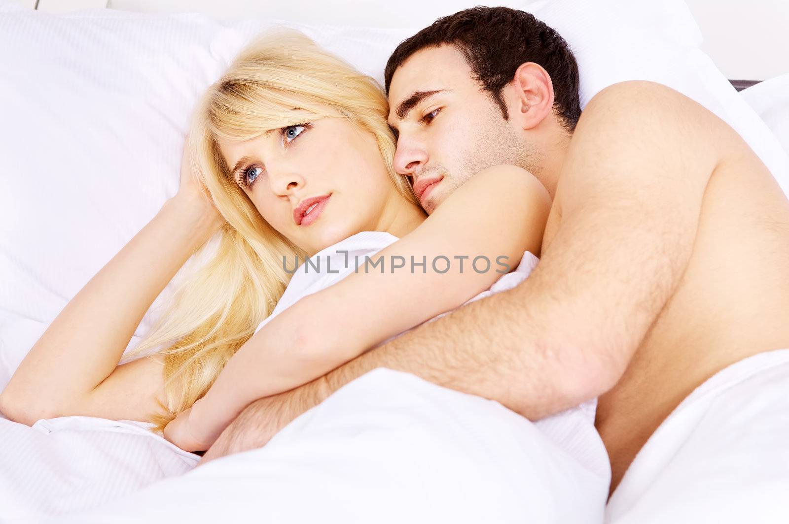 Young couple in bed, he embracing her, focus on woman