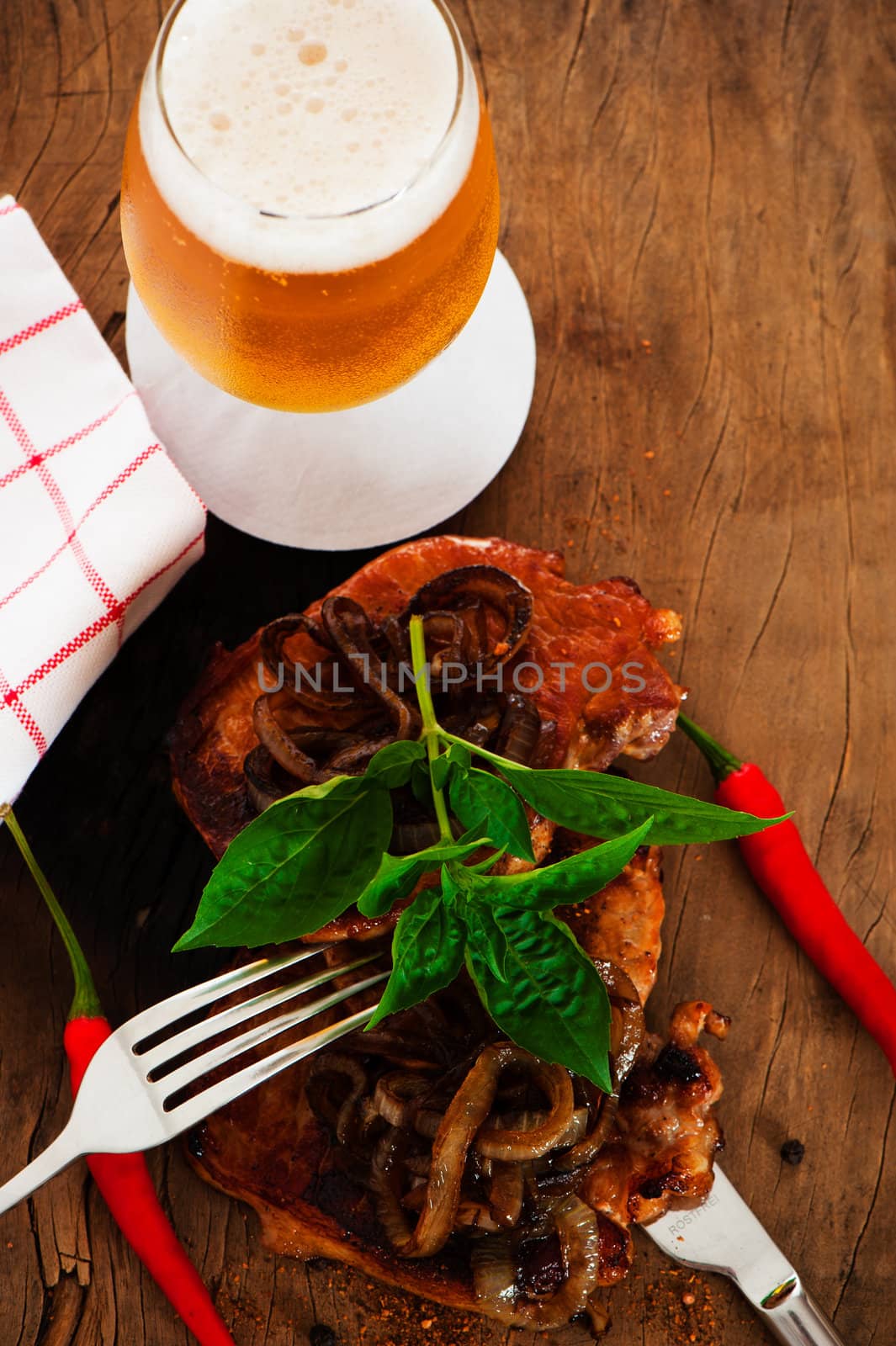 View of some pieces of spicy fried meat with onion on a wooden underground chili  pepper and beer as decoration