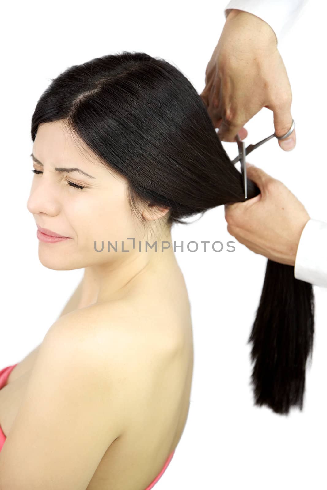 Beautiful woman keeping her eyes closed scared while hairdresser cuts her long ponytail by fmarsicano