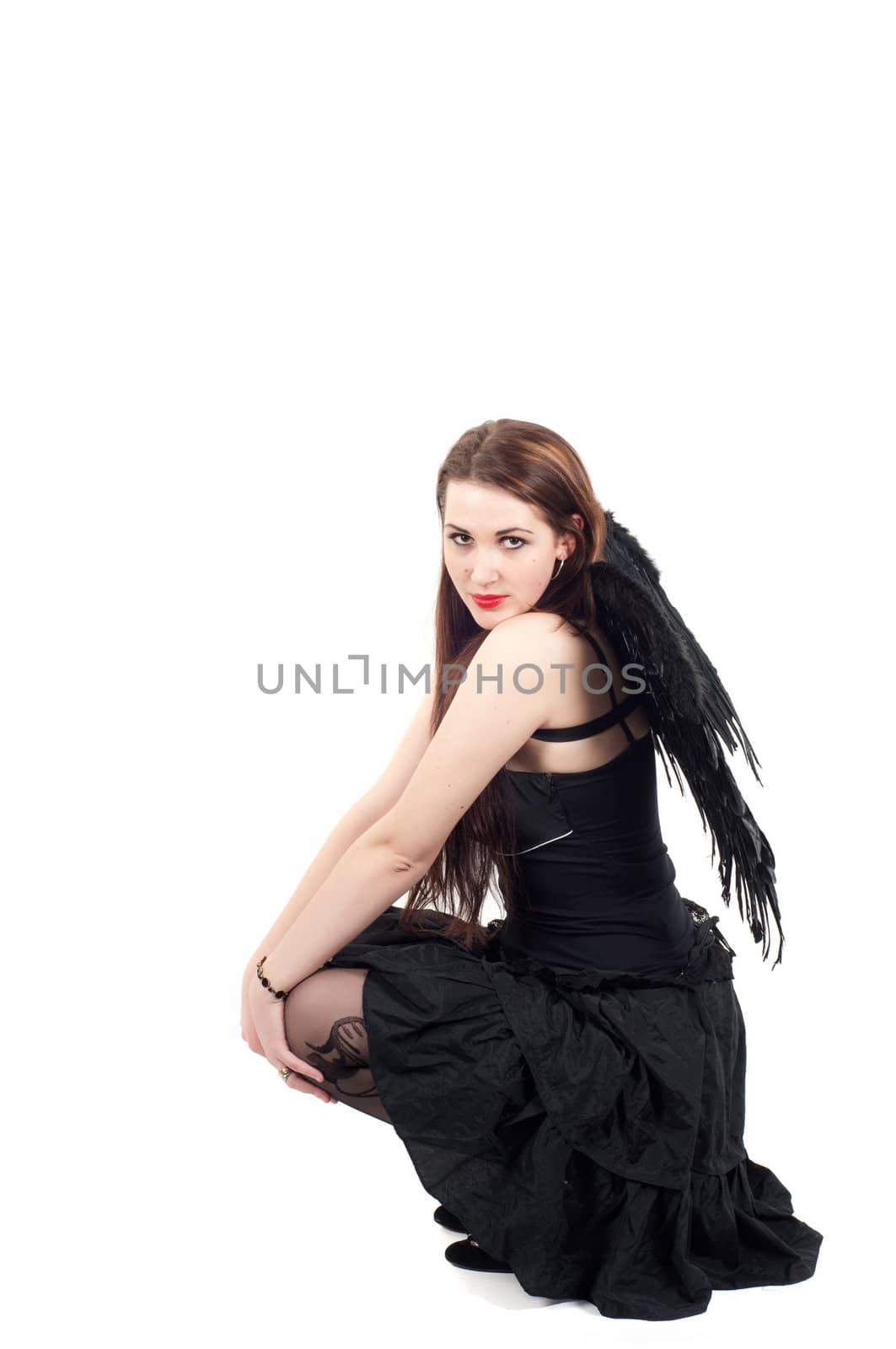 Beautiful brunette woman with black wings sitting in studio on white