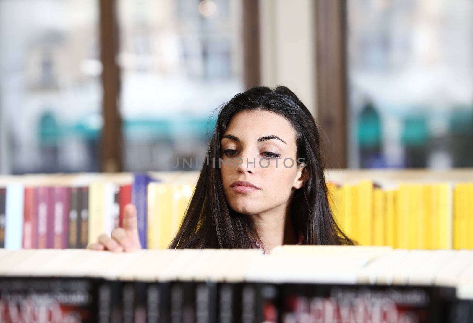 pretty young woman looking for a book in a bookstore by stokkete