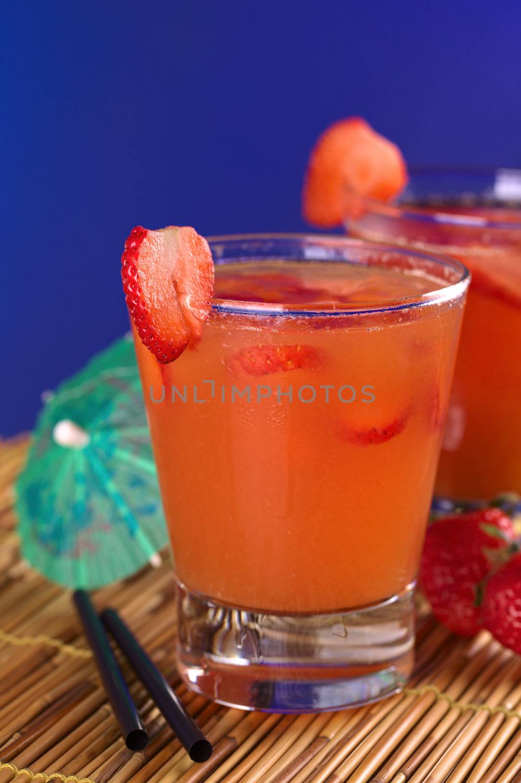 Peruvian cocktail called Pisquina made of pisco, passion fruit and cranberry juice, fresh strawberries, sugar and ice (Selective Focus, Focus on the front rim of the glass and the front of the strawberry slice on the rim)