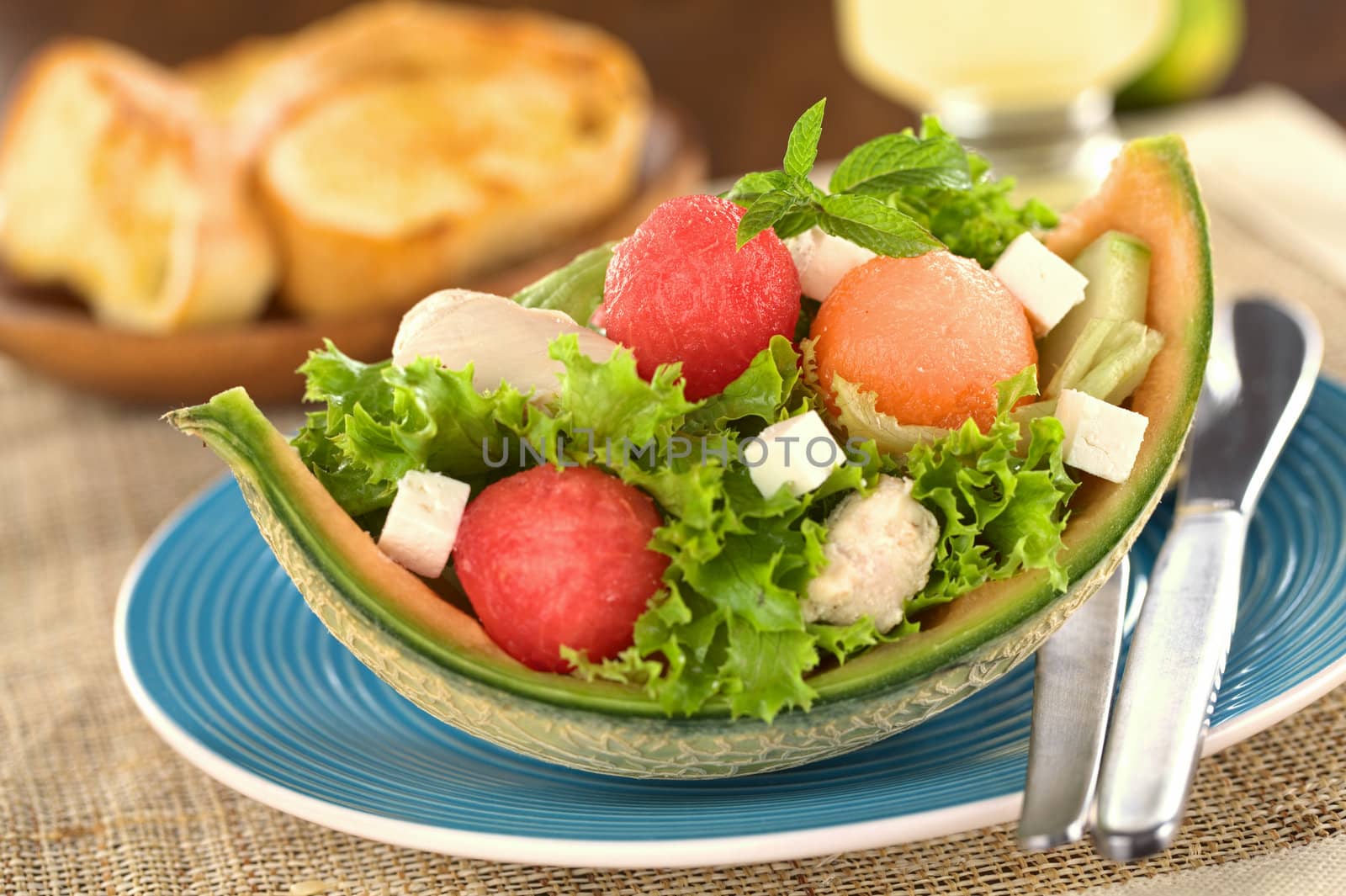 Fresh salad made of watermelon, cantaloupe melon, chicken, cucumber, cheese and lettuce (Selective Focus, Focus on the front of the mint leaf and the two melon balls below it)