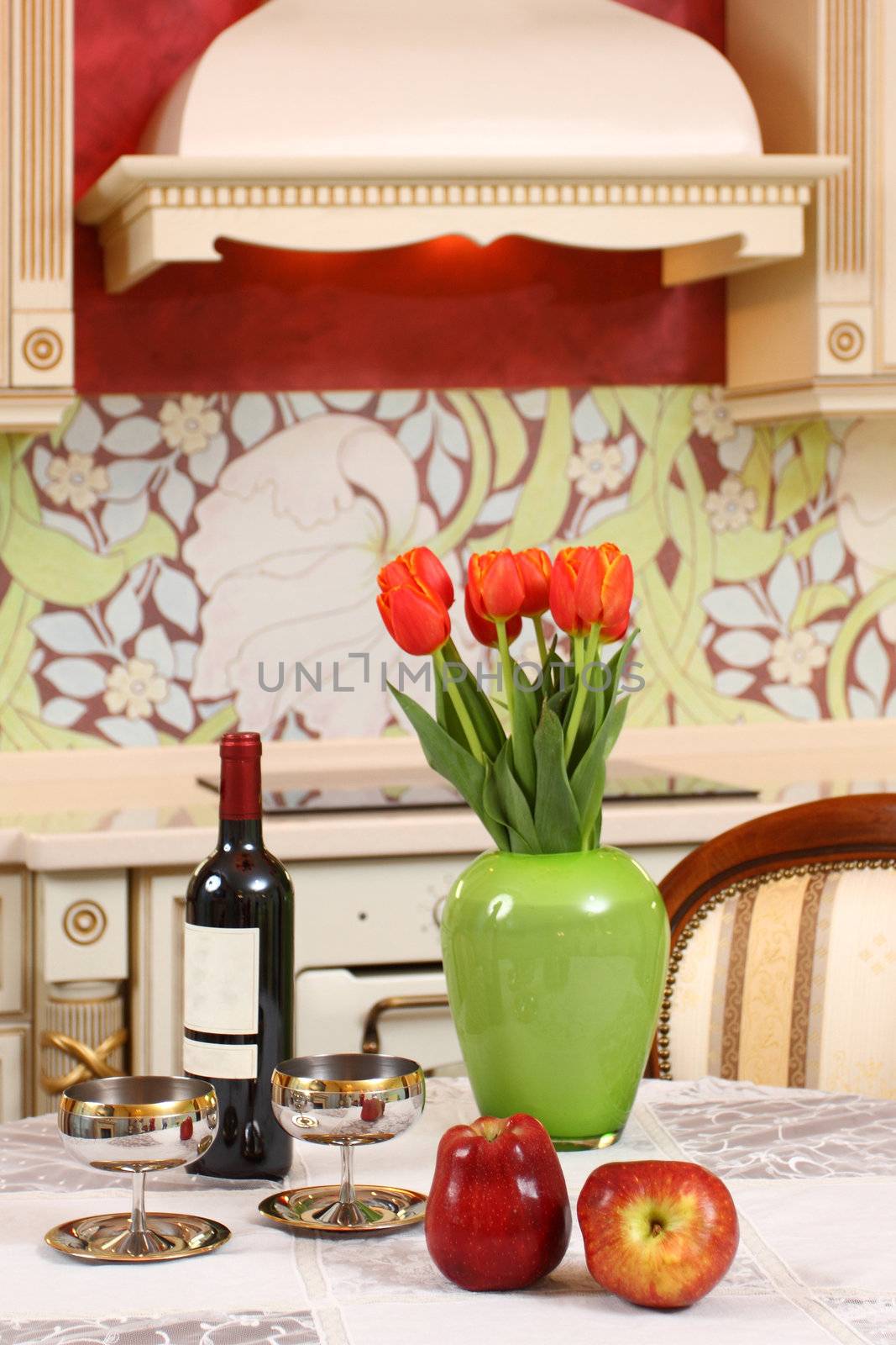 the wine bottle, two glasses, apples and bouquet of tulips in a green vase on a kitchen table