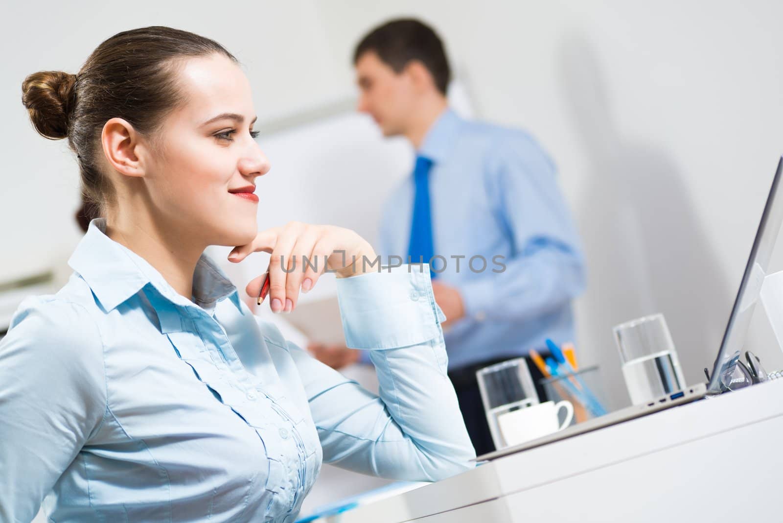 Business woman thinks for a laptop in the office, in the background debating colleagues