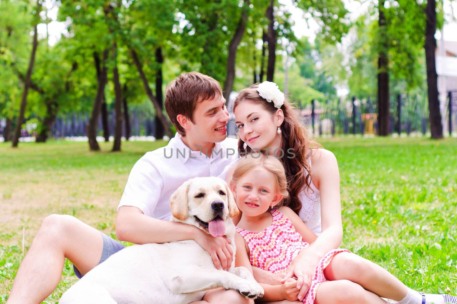 Happy young family with Labrador is resting in the park