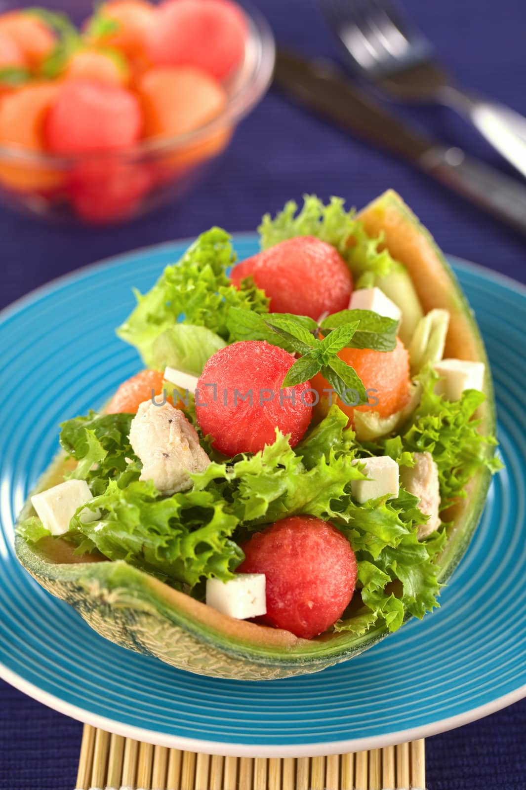 Fresh salad made of watermelon, cantaloupe melon, chicken, cucumber, cheese and lettuce (Selective Focus, Focus on the front of the mint leaf and the watermelon ball below it)