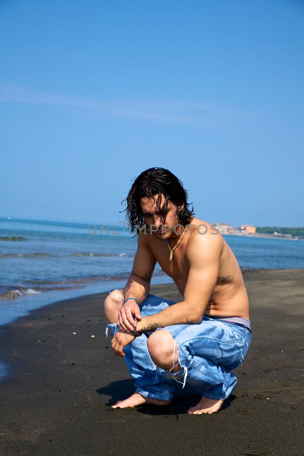 Fashion model male on the beach relaxing and thinking