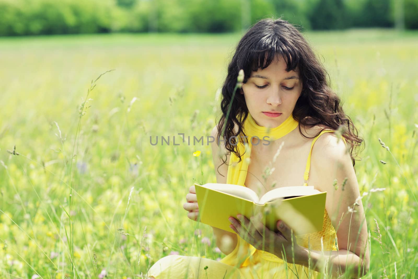 beautiful young woman reading book in a field full of yellow flowers