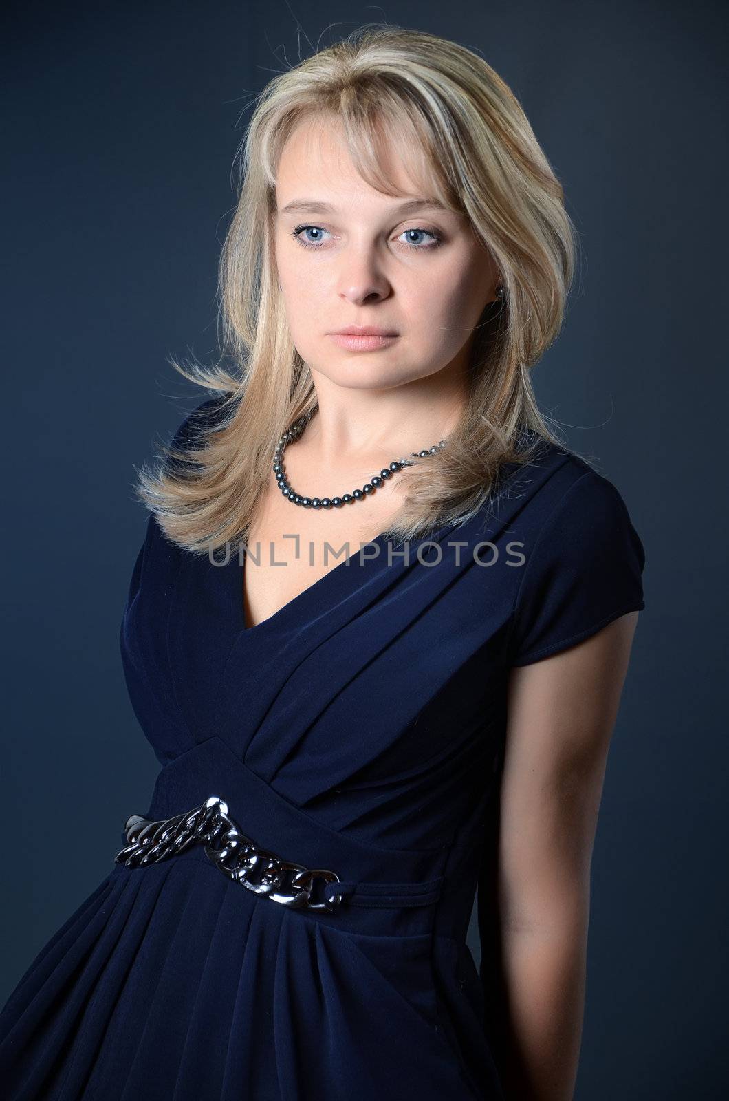 attractive young blond girl dressed with blue evening dress looking at the camera against grey background