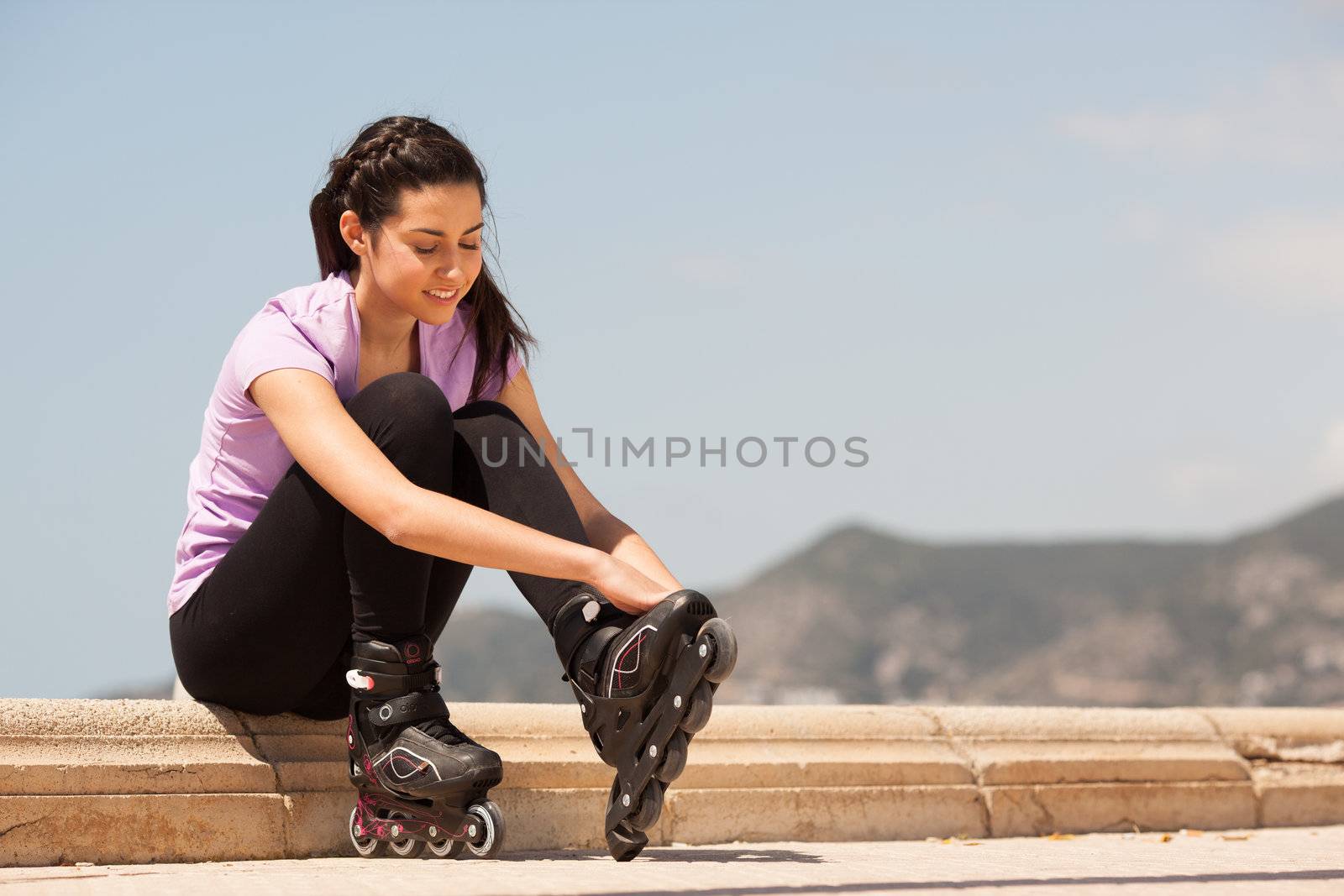 Girl going rollerblading sitting putting on inline skates outdoors