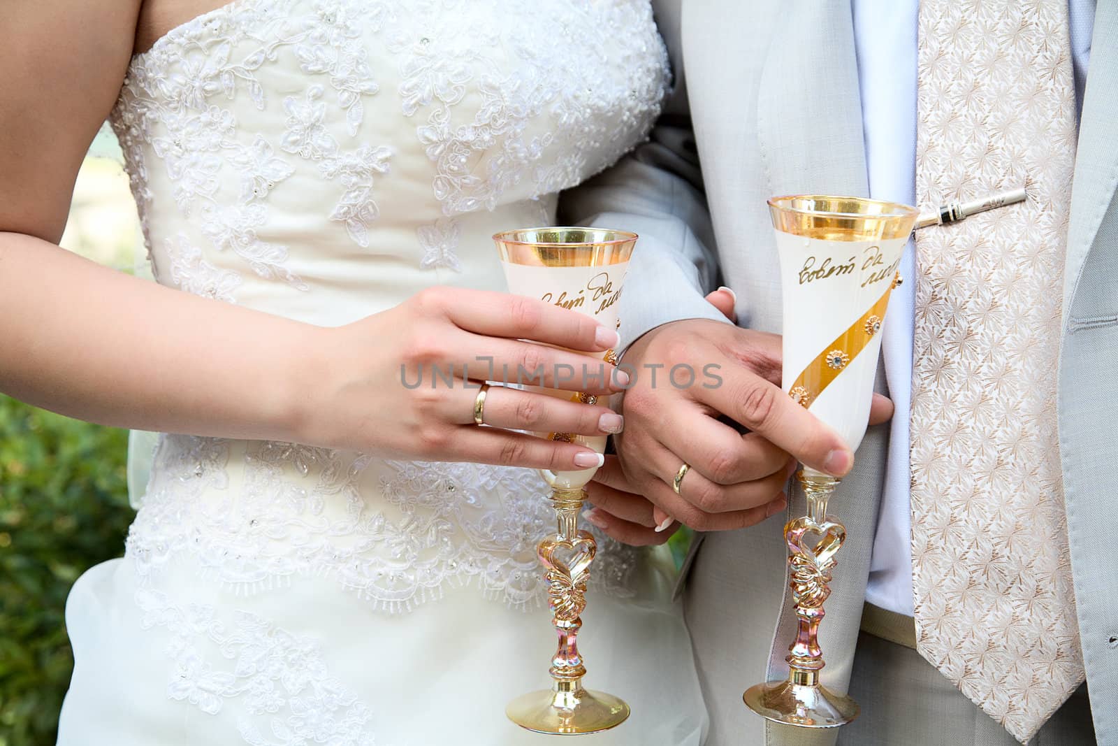 The groom and the bride hold glasses with schampagne close up