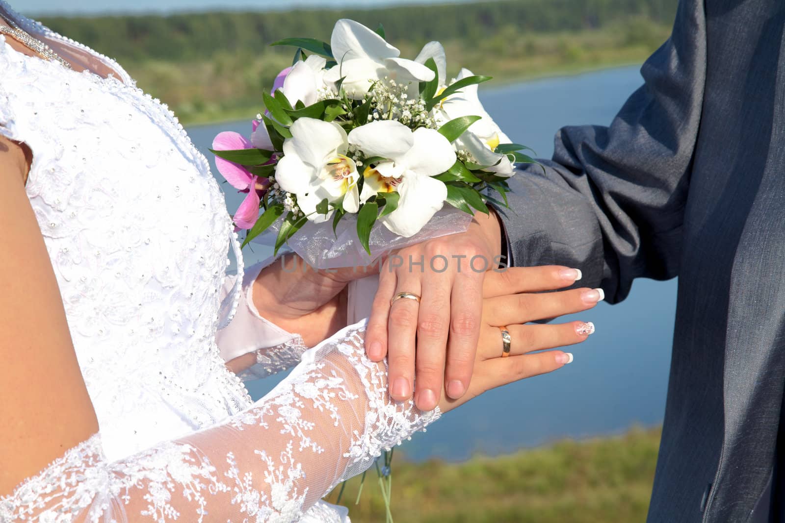 Hands and rings with wedding bouquet against a river