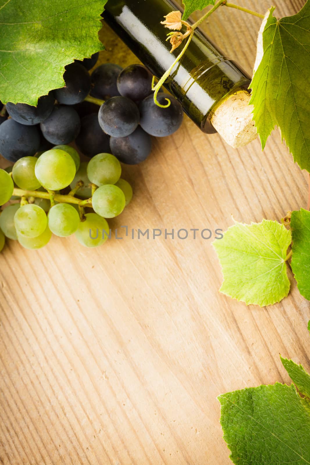 bottle of wine with leaves and grapes on wooden table