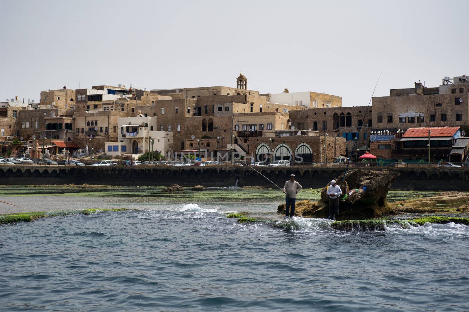 Fishers on the view of ancient crusader fortress in the town of Akko, Israel