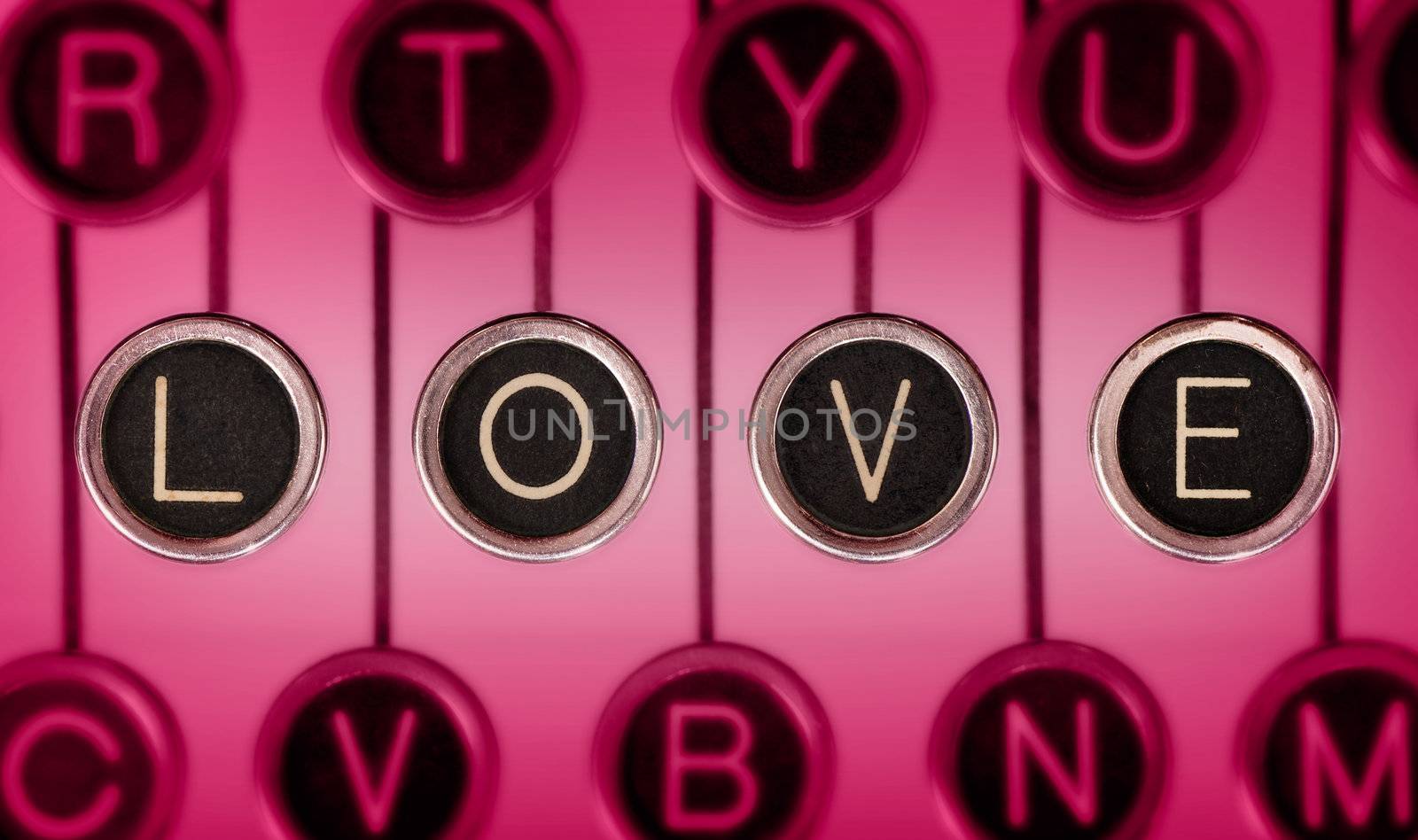 Close up of old typewriter keyboard with scratched chrome keys that spell out LOVE. Lighting and focus are centered on LOVE.
