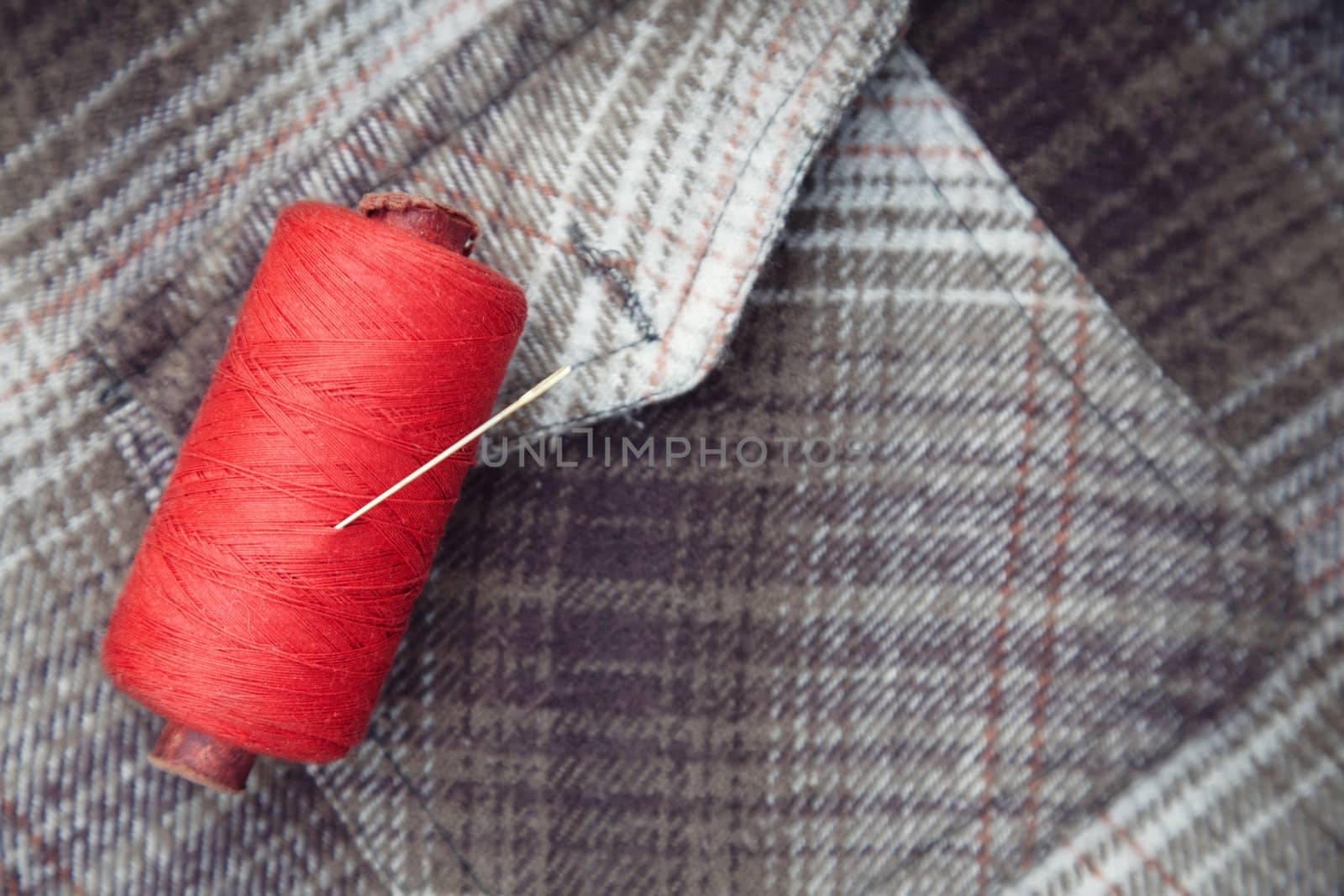 Red sewing spool with needle on a flannel fiber. Close-up photo