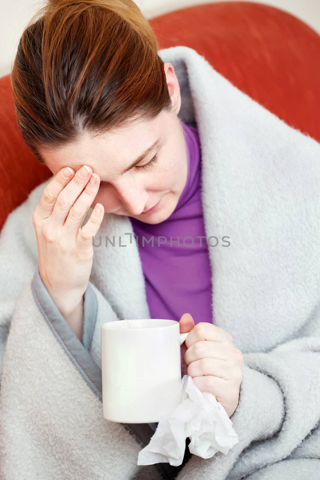 A young sick woman having headache, holding cup of tea and handkerchief